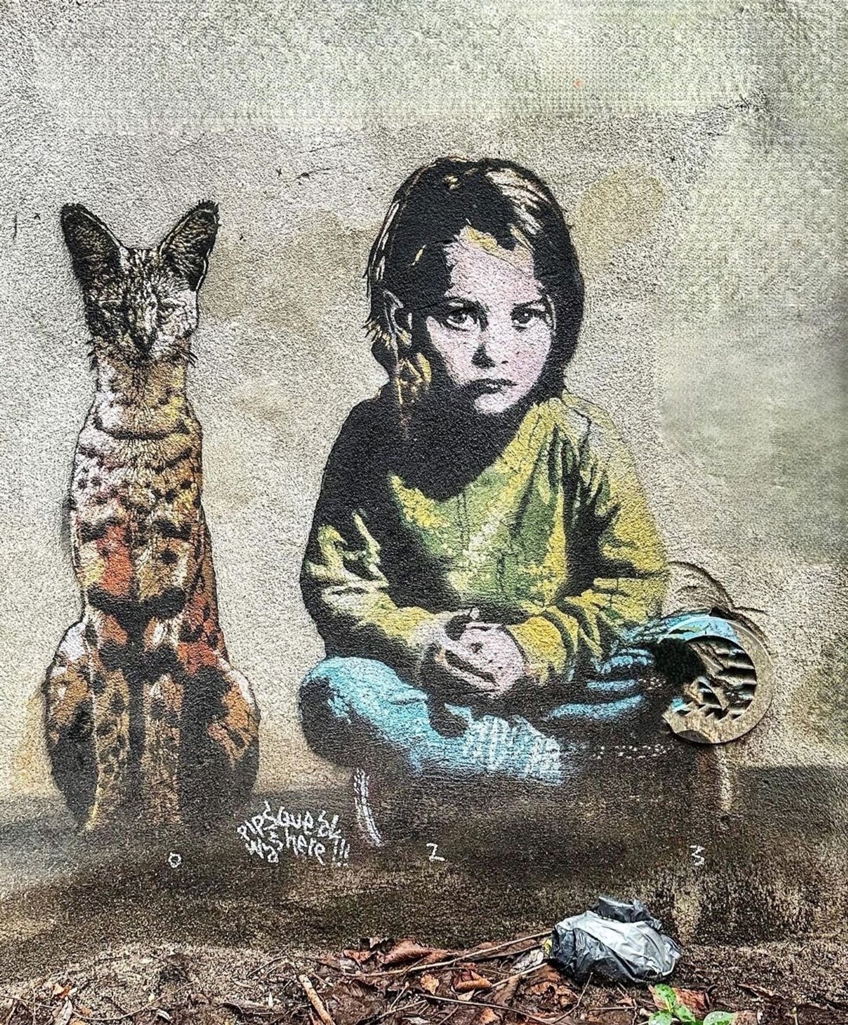 Streetartwall. A charming little mural with a little girl and a wild cat was sprayed/painted on a beige-colored wall. The brown-haired girl is sitting cross-legged on the floor wearing a light green sweater and blue pants. Her arms are folded in her lap. A proud black/yellow/orange wildcat with a small head sits upright next to her. Both are looking at the viewer.
Info: Pipsqueak was here!!! is an Amsterdam-based artist duo driven by a strong passion for all life on planet earth. Animals are not metaphorical placeholders for humans, they are animals. The children are children.