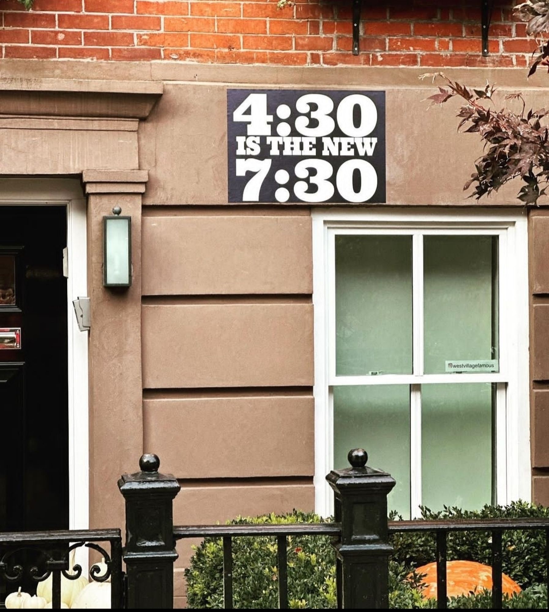 Streetart. A black poster with white text is attached to a brown house wall with. Above a window is written: "4:30 Is The New 7:30"