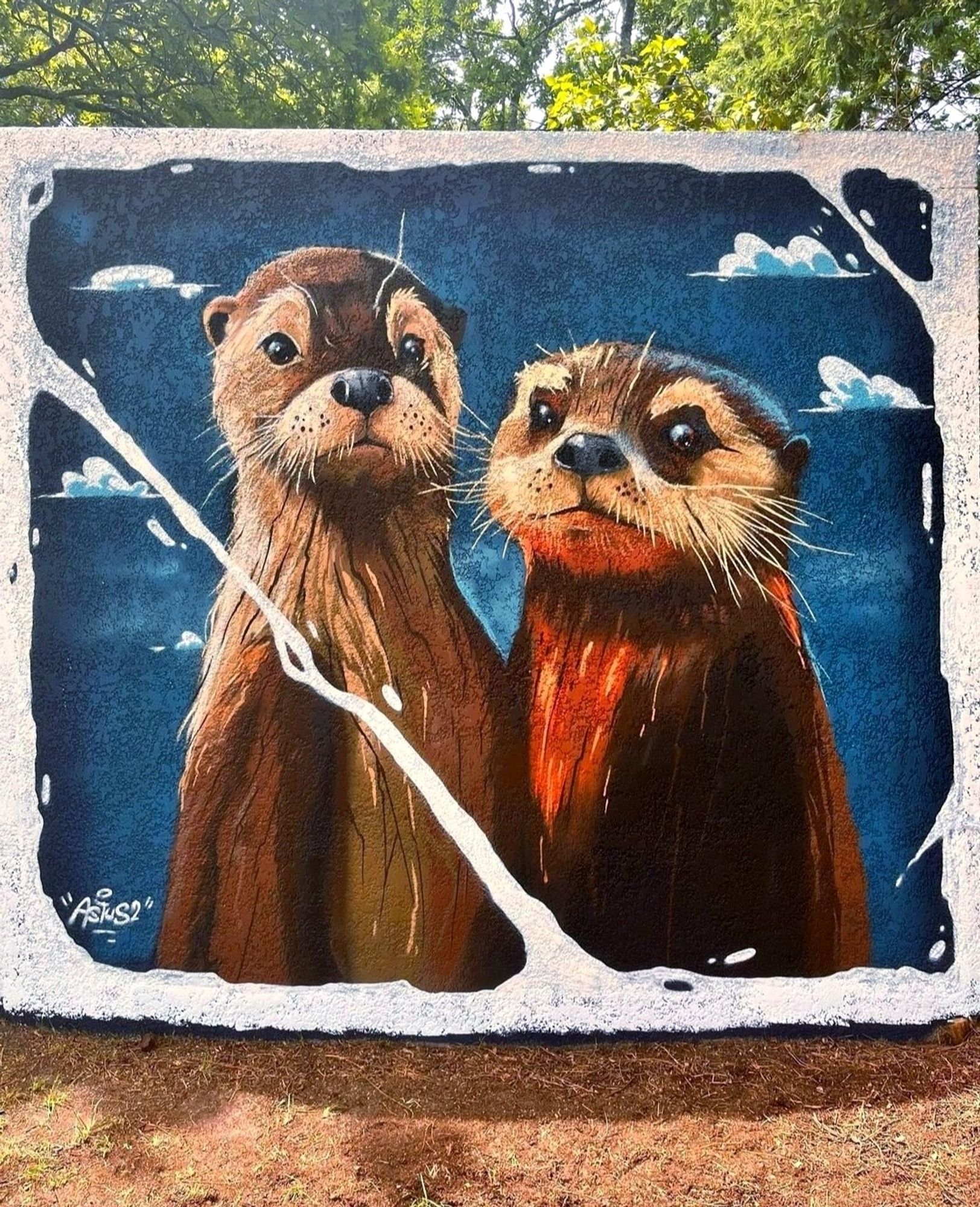 Streetartwall. As part of a festival, two cute otters were sprayed/painted on the outside walls of square electrical transformer houses. It is one of three murals showing otters in different situations on three of the sides. One under water, one on the shore and this one with a view of the passer-by. The two are half depicted and standing next to each other. Two fluffy brown creatures with large black eyes, small noses, small ears and slender furry bodies. The background is a blue, cloudy sky. Both have a self-confident to interested expression and are simply very, very cute.
Info: Jerome Salas alias Astus² is an artist from Perpignan. His style is characterized by a mixture of bold colors and daring lines.