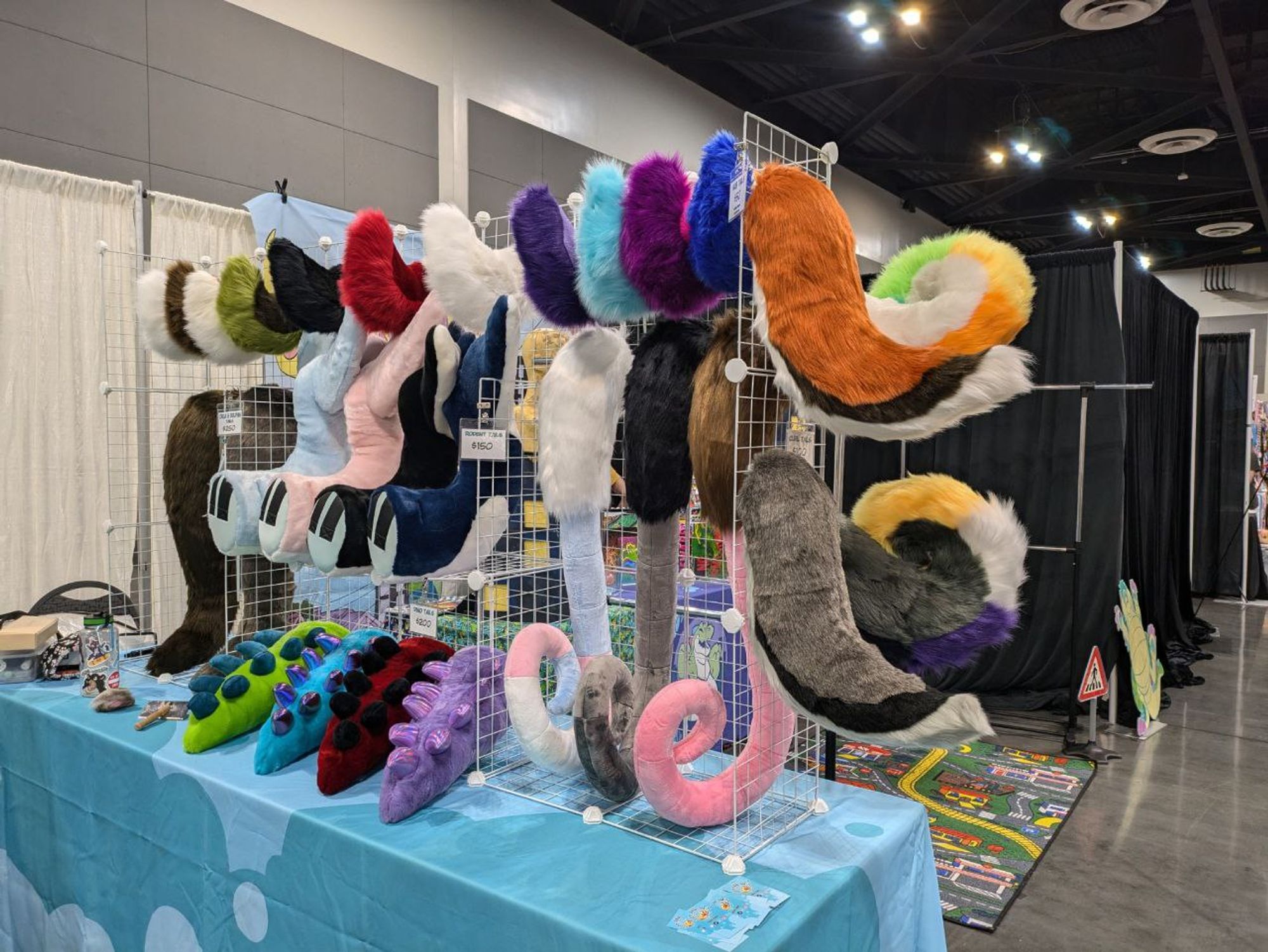 Lion Paw Suits dealer table at AFC 2024 featuring an array of colorful hand and feet paws as well as tails and accessories.