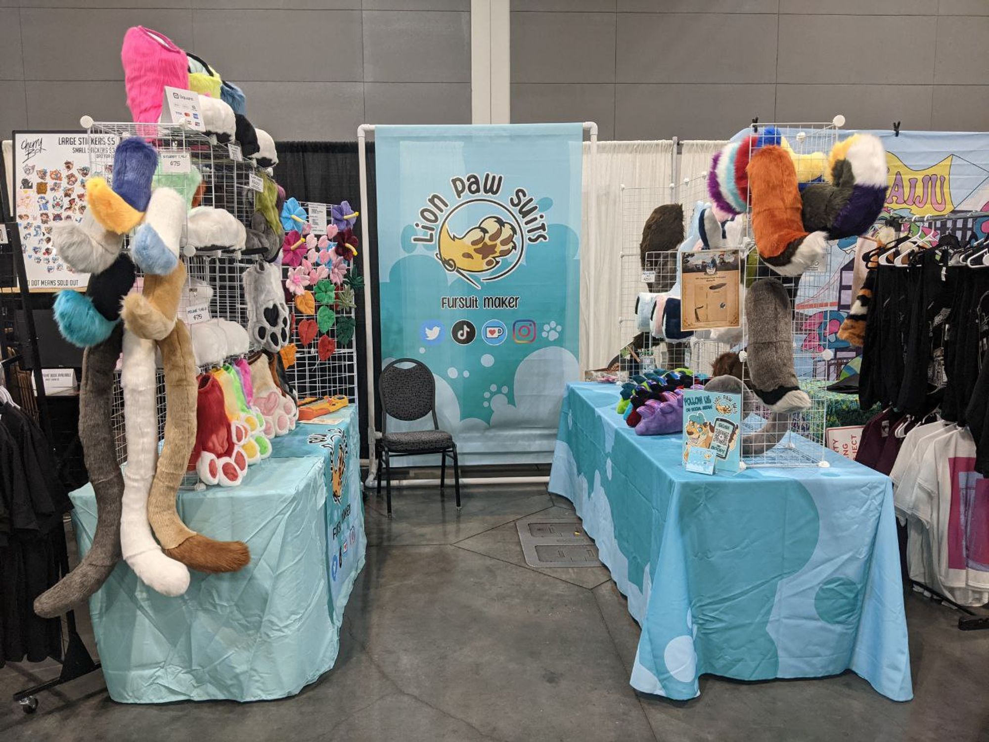 Lion Paw Suits dealer table at AFC 2024 featuring an array of colorful hand and feet paws as well as tails and accessories.