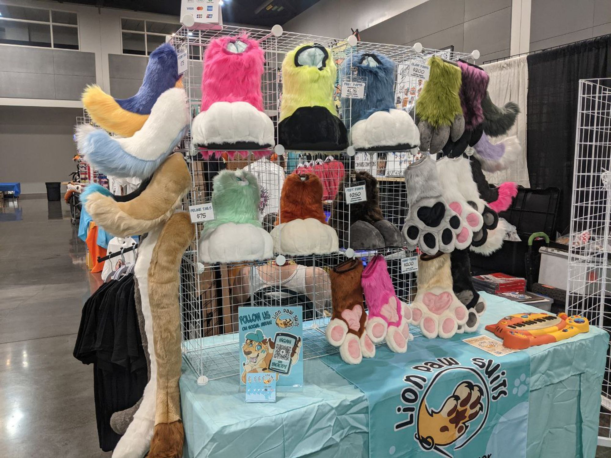 Lion Paw Suits dealer table at AFC 2024 featuring an array of colorful hand and feet paws as well as tails and accessories.