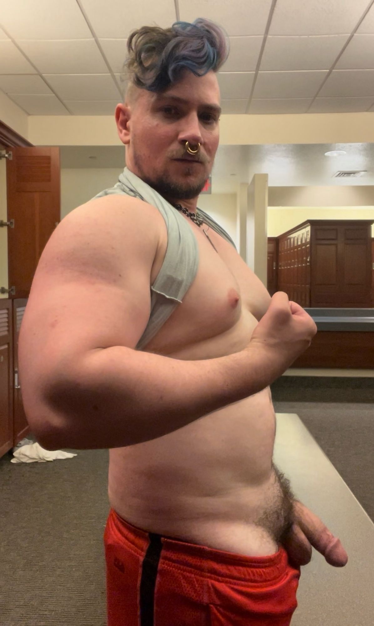 Nude gym selfie, flexing arm, side view, soft cock poking out of gym shorts