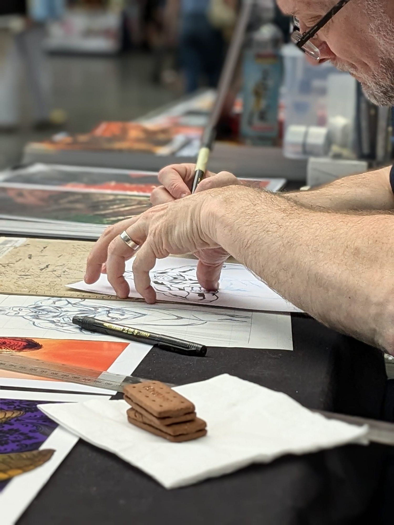 Comic artist drawing, there are biscuits to fuel his art in the foreground.