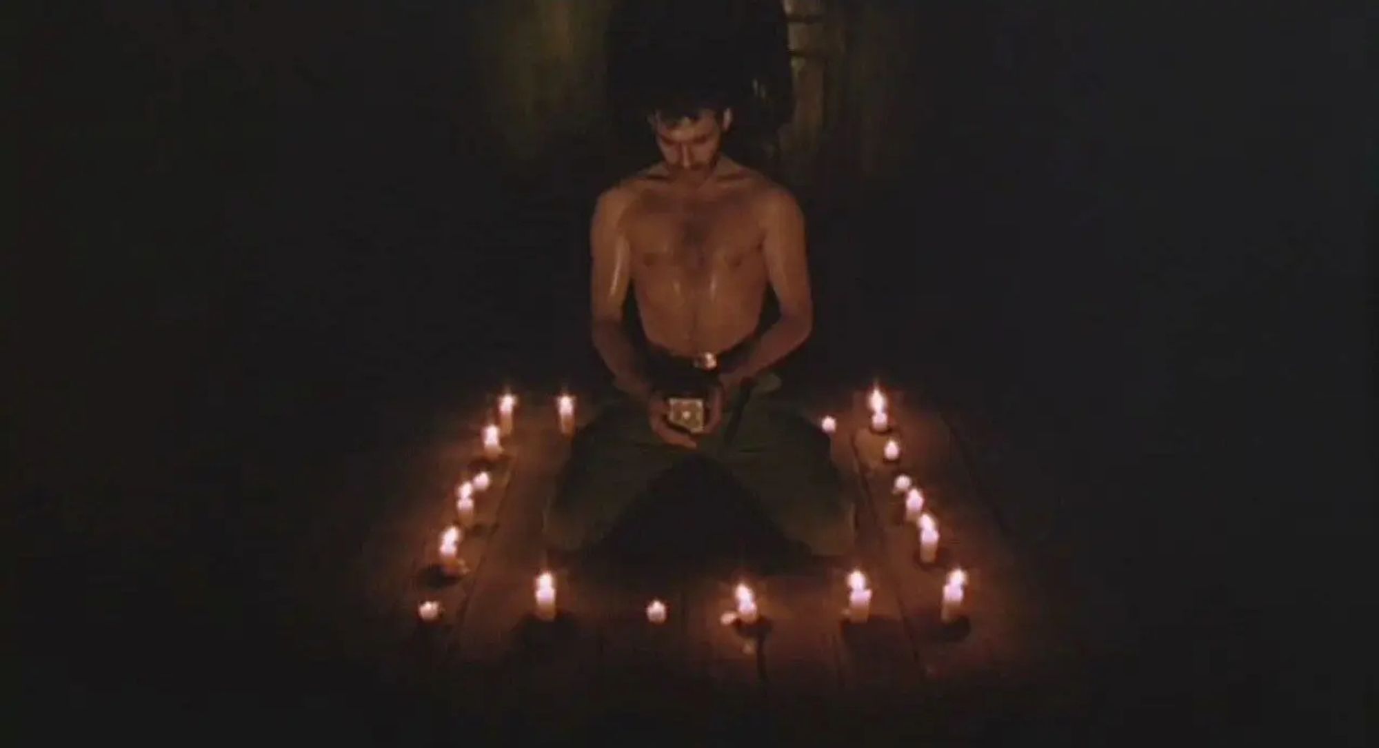 Frank Cotton (Sean Chapman) from *Hellraiser* (1987) on his knees surrounded by burning candles with the Lament Configuration box in his hands