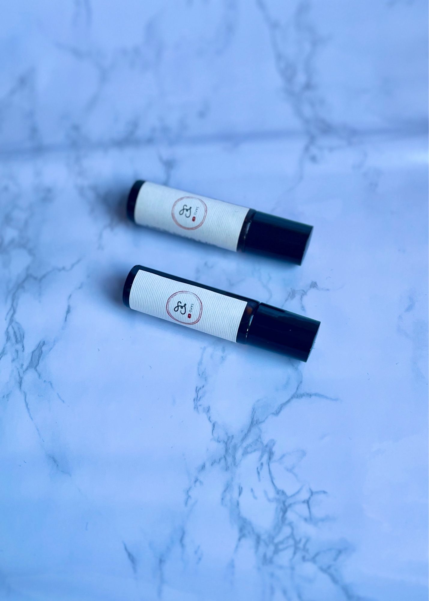 two perfume oils from our upcoming winter collection sit on a pale faux marble backdrop