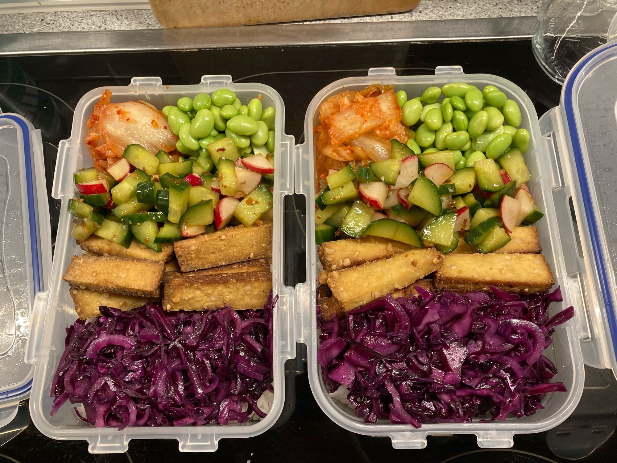 Zwei Vorratsdosen mit diversen Salaten, Tofu, Edamame und Kimchi, darunter Reis