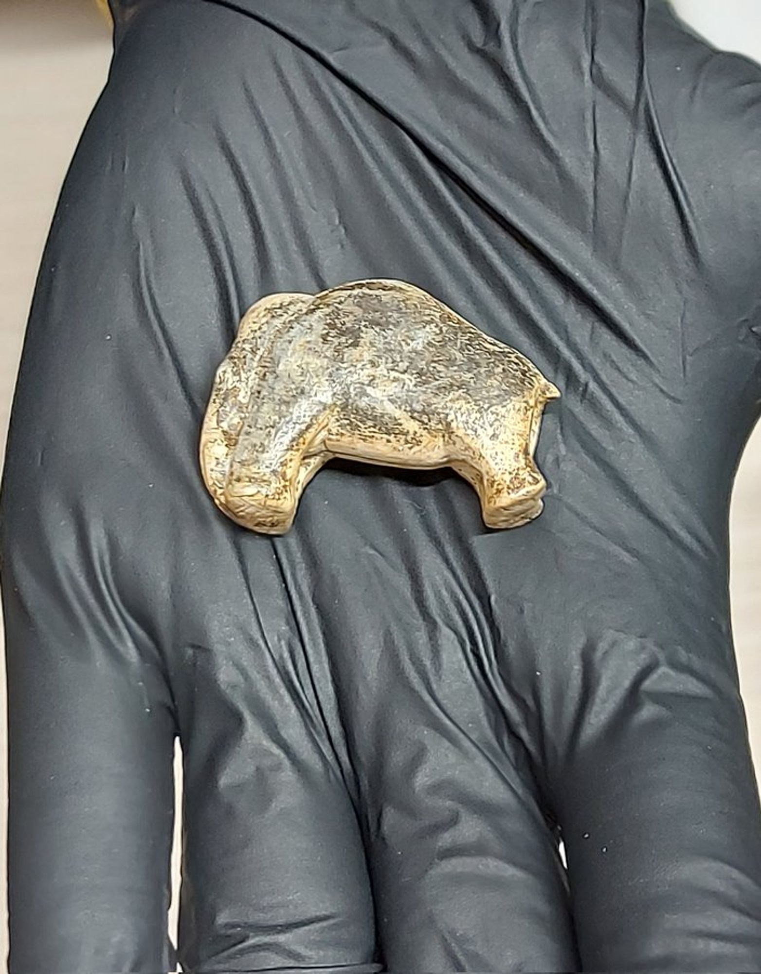 The picture shows the small ivory figurine of a mammoth. It lies on a gloved hand.