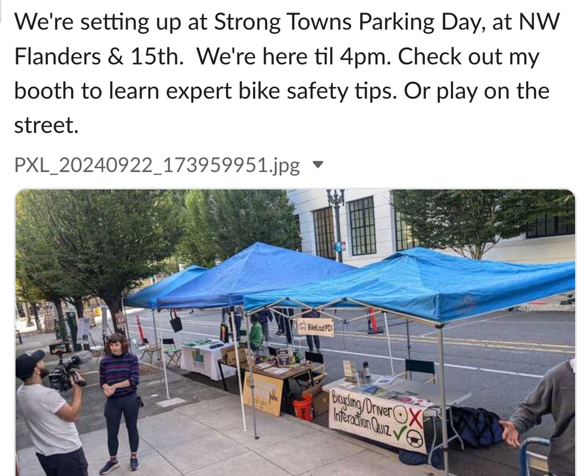 Booths lining the street with people talking to each other. The text says "We're setting up at Strong Towns Parking Day, at NW Flanders & 15th.  We're here til 4pm. Check out my booth to learn expert bike safety tips. Or play on the street."