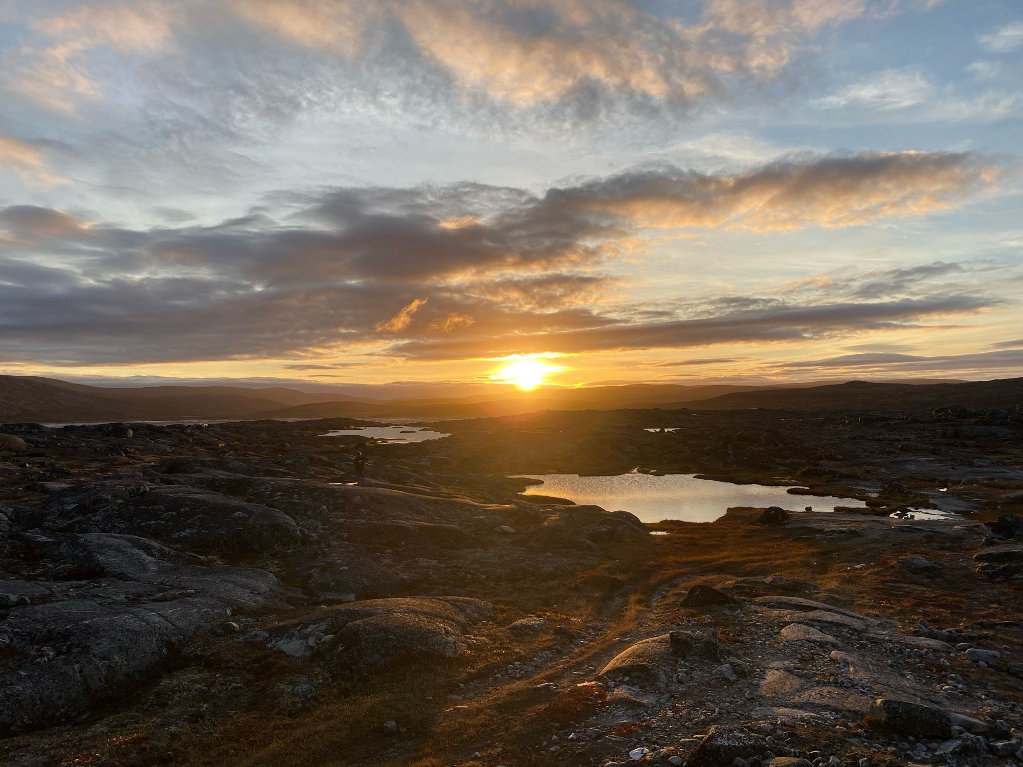 Sunset over rocks, tundra, and ponds.