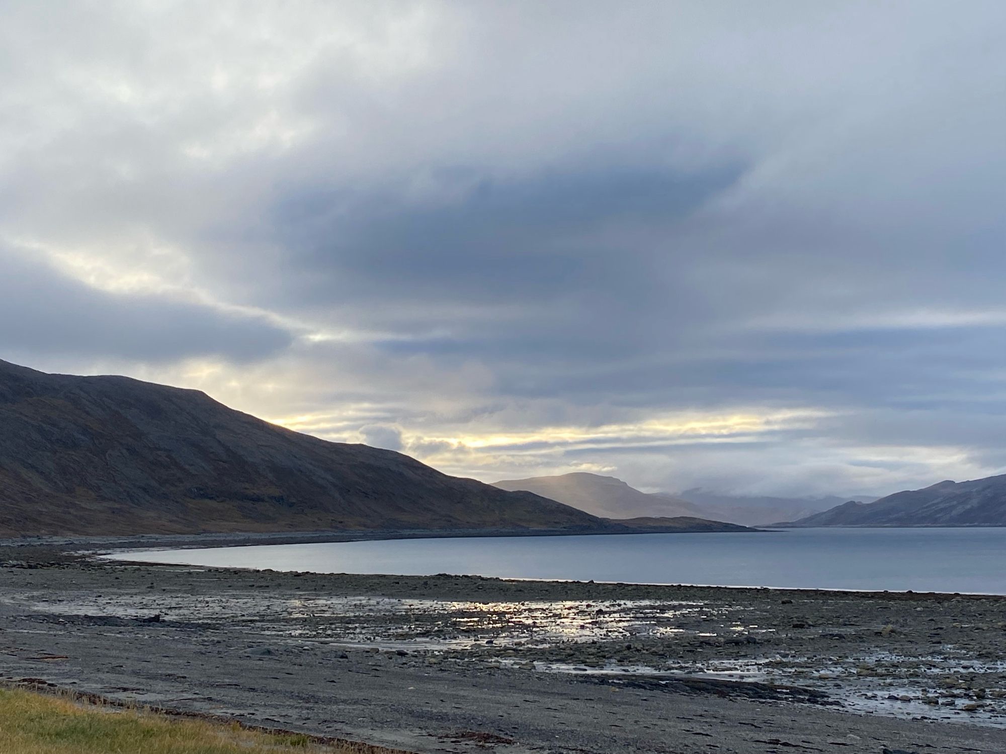 Misty mountains beyond a calm bay.  Rocky shore at low tide.