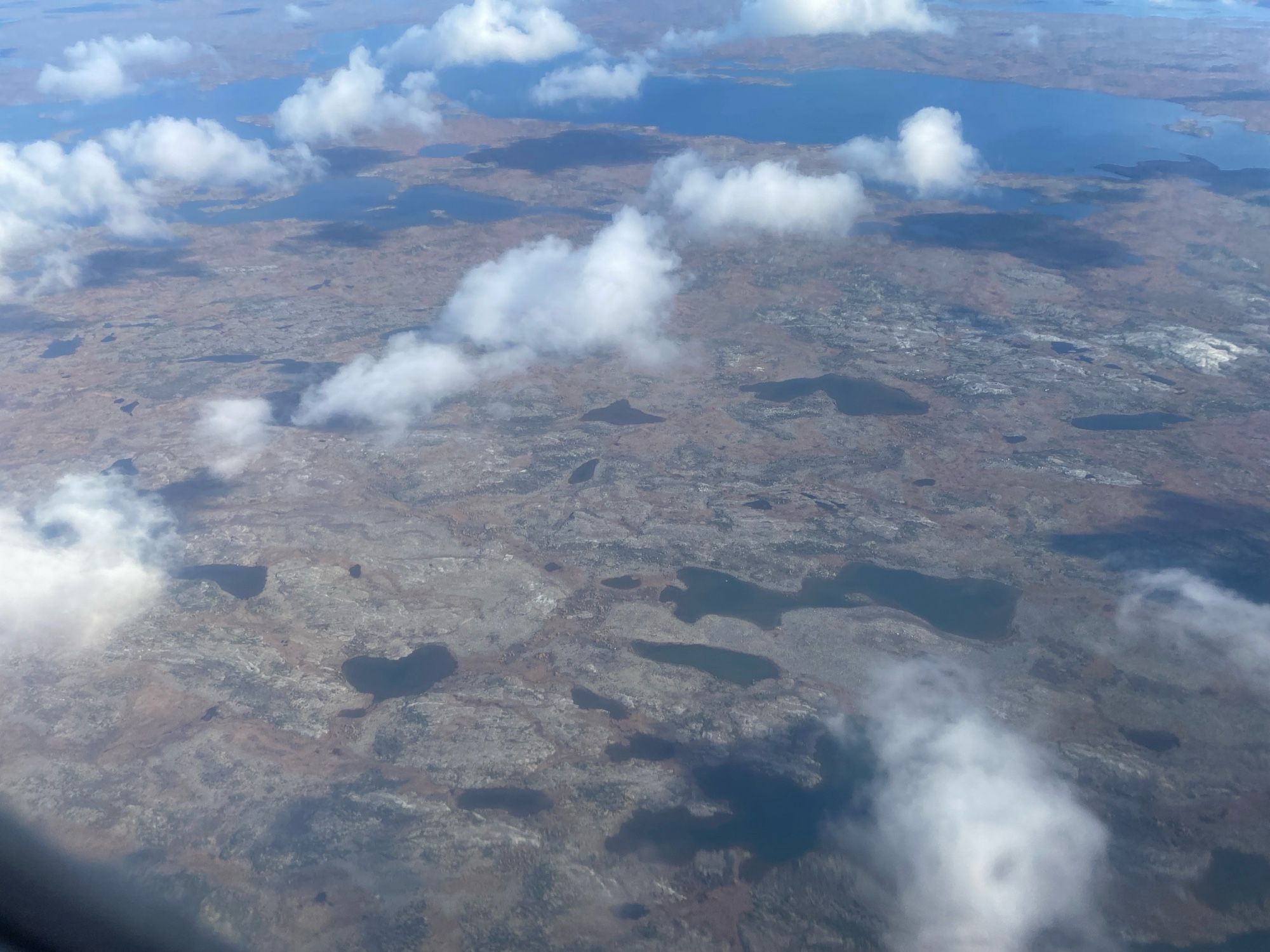 Low cumulus over tundra and lakes.  The trees are hard to see— they are Tamaracks, which turn yellow-brown in the fall, and blend in with the brown tundra.  The trees are in low protected spots and are only 20-30 feet tall.