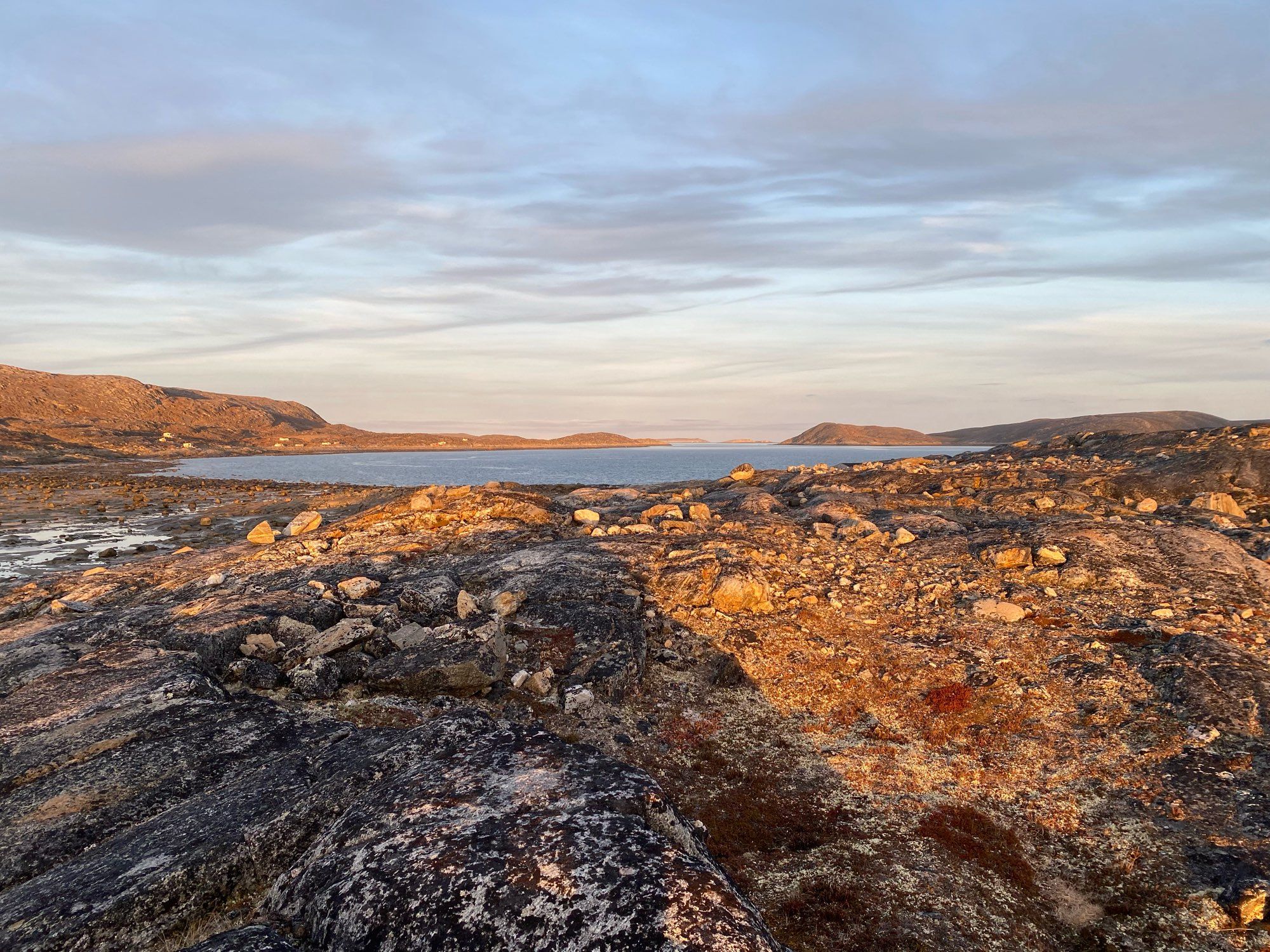 Looking over rocks and tundra towards a bay with hunting shacks in the background.  Evening light adds a warmth to the crisp air.