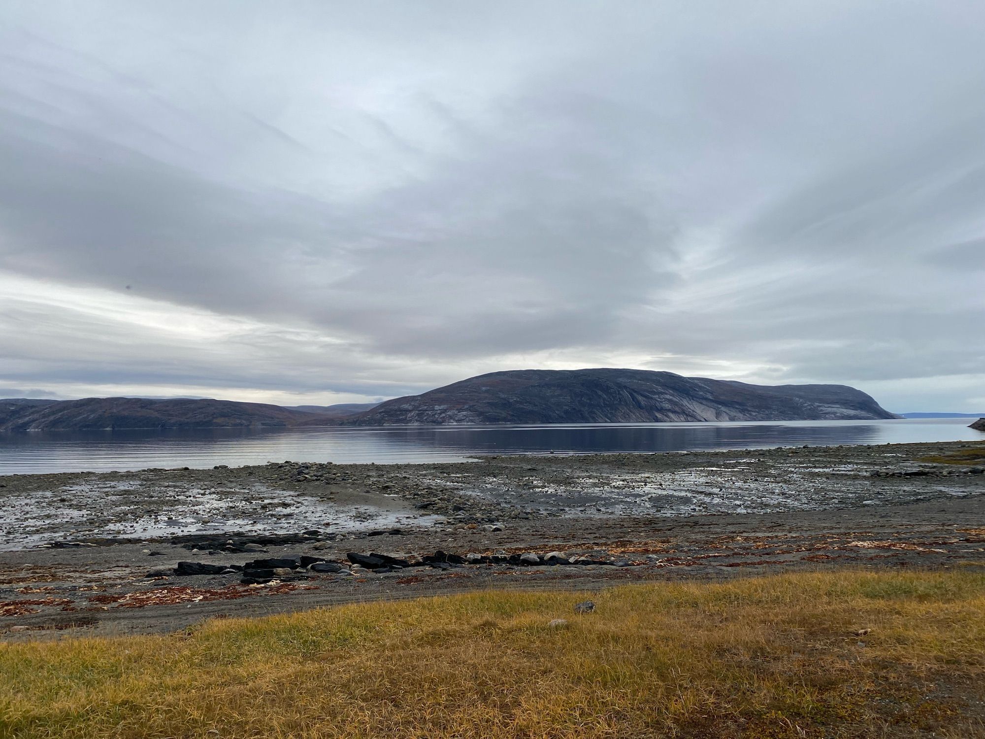 Grassy shore with rocks at low tide.  Distant shore three miles away shaded by low stratus.