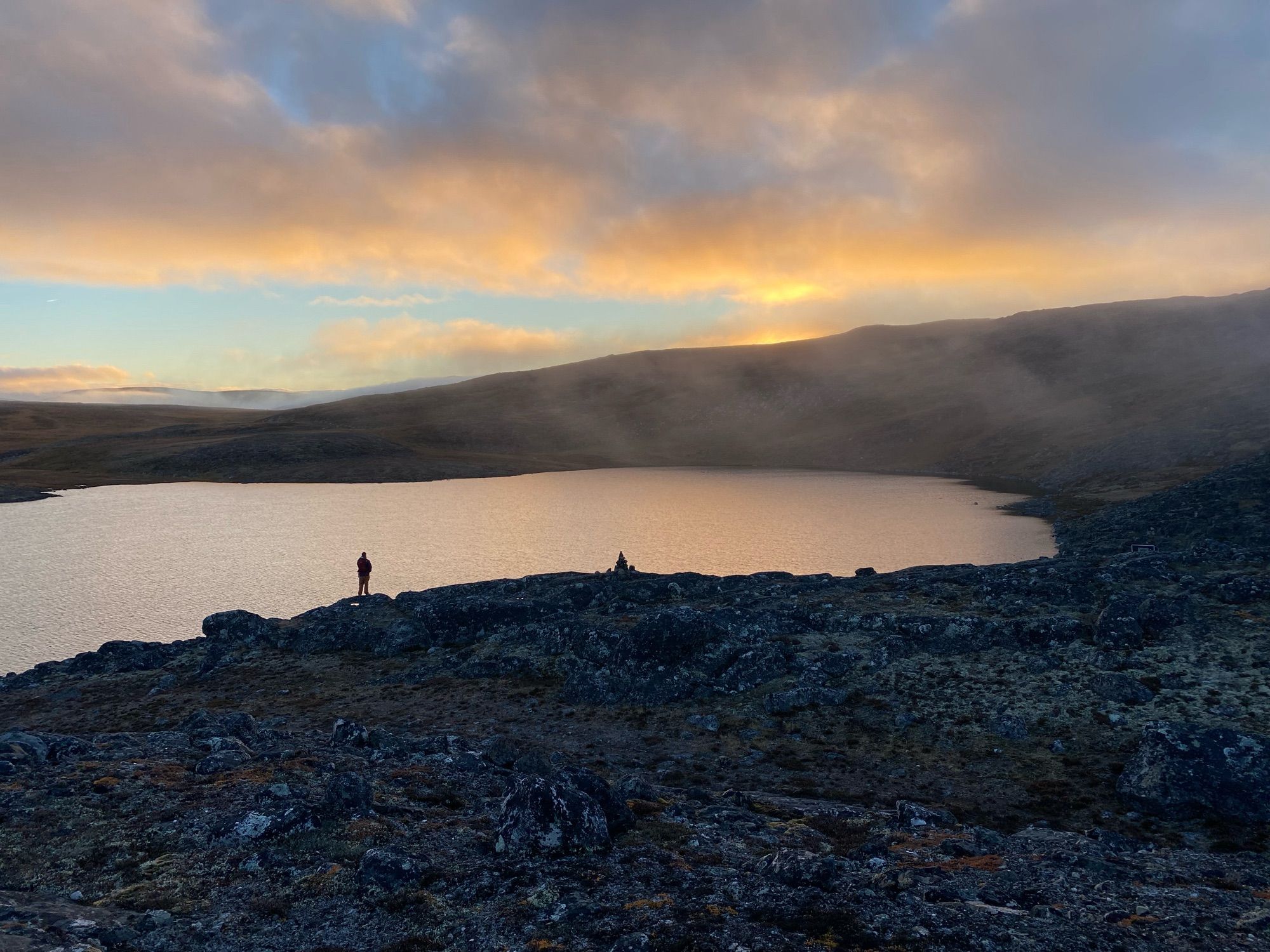 Yellow lit low cumulus and mist over a lake surrounded by rocky hills.