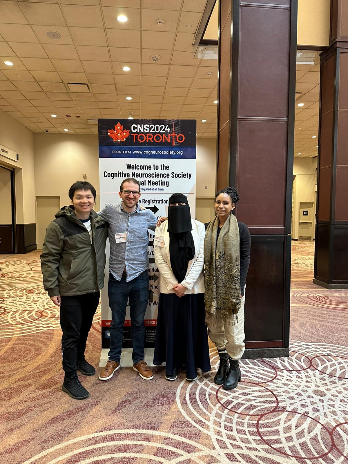 @huangjiawen.bsky.social, craig poskanzer, @raheemajavid.bsky.social, and @hartwakeland.bsky.social stand in front of a poster that reads: “CNS 2024 Toronto” “Welcome to the Cognitive Neuroscience Society Annual Meeting”