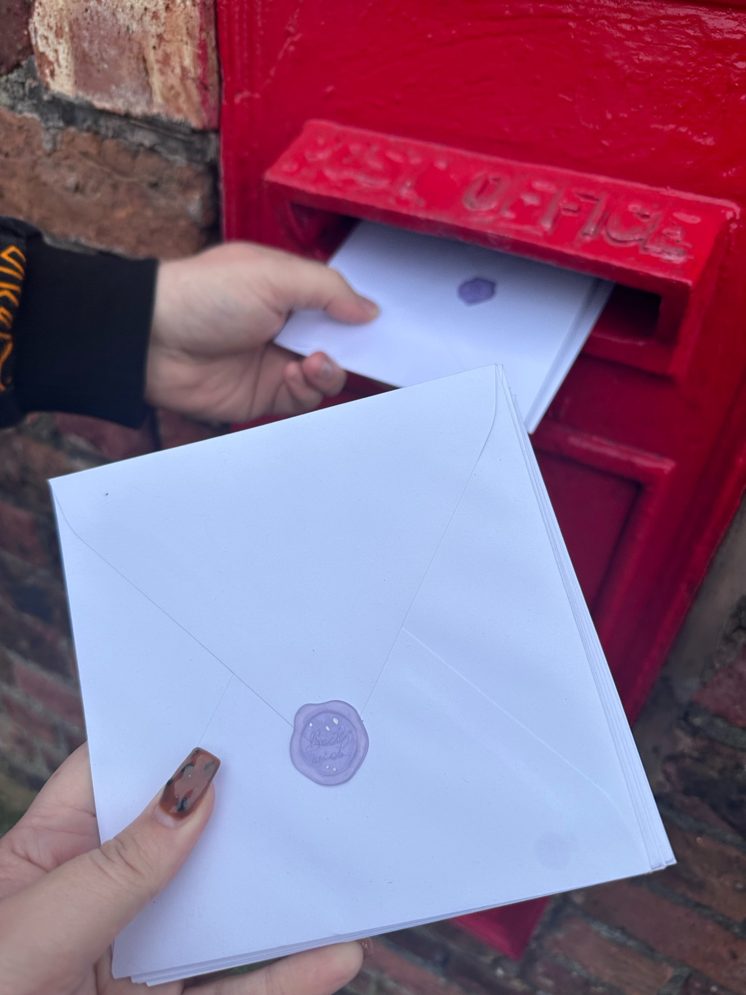 Charlotte and Stu holding envelopes about to post them in a postbox 