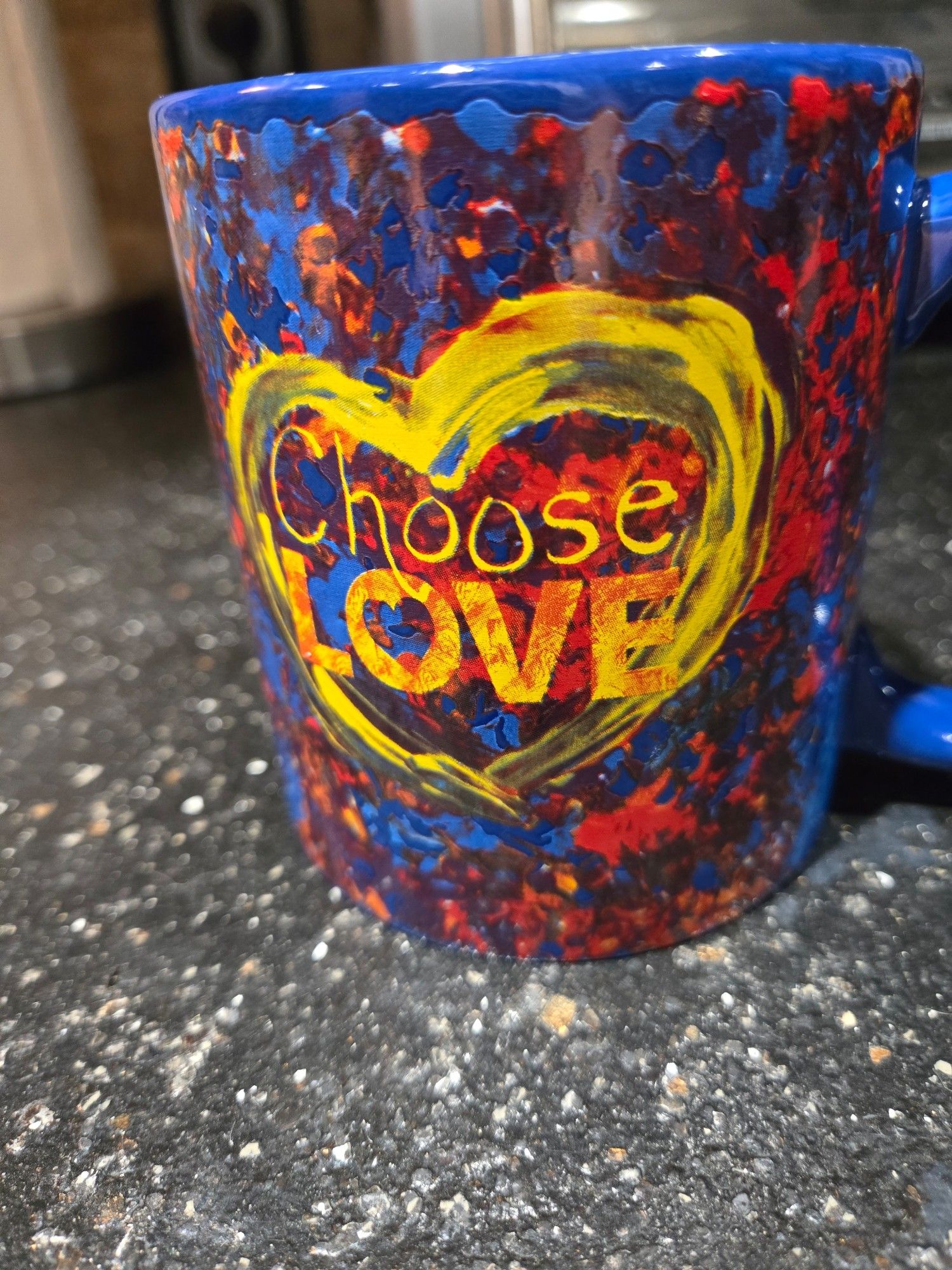 Penzey's coffee mug with yellow "Choose Love" inside of a heart on a bright blue and red "tie dyed" background.