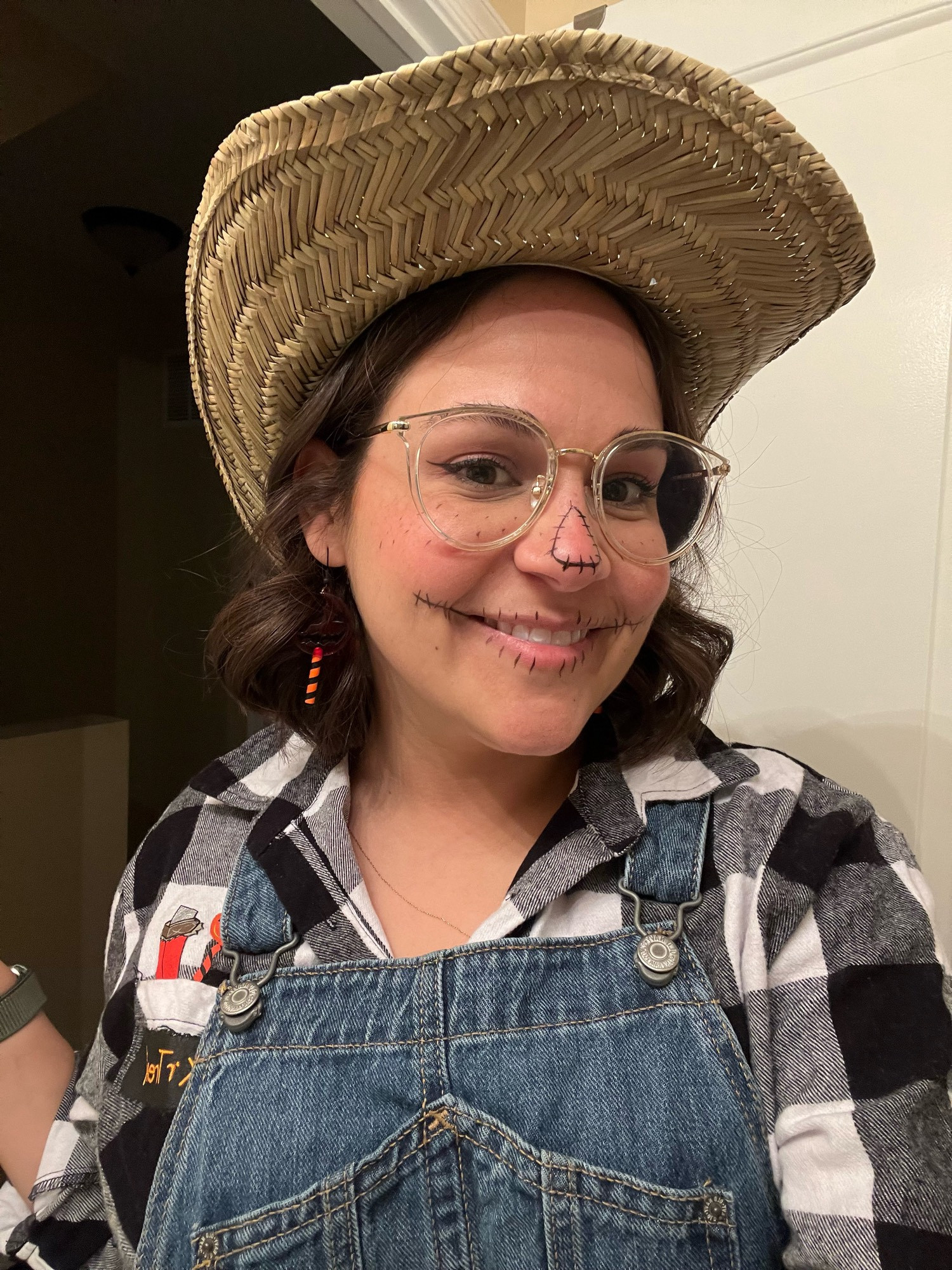 Jamie dressed as a scarecrow with a hat, overalls, and a flannel shirt. she has makeup on her face to look like a scarecrow!