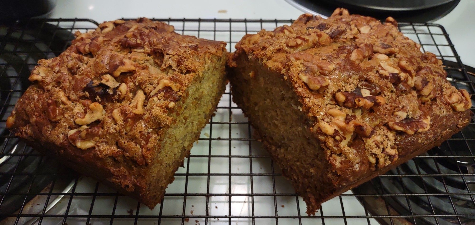 Banana banana bread loaf, cut in half on a cooling rack, with lightly candied walnuts on top.