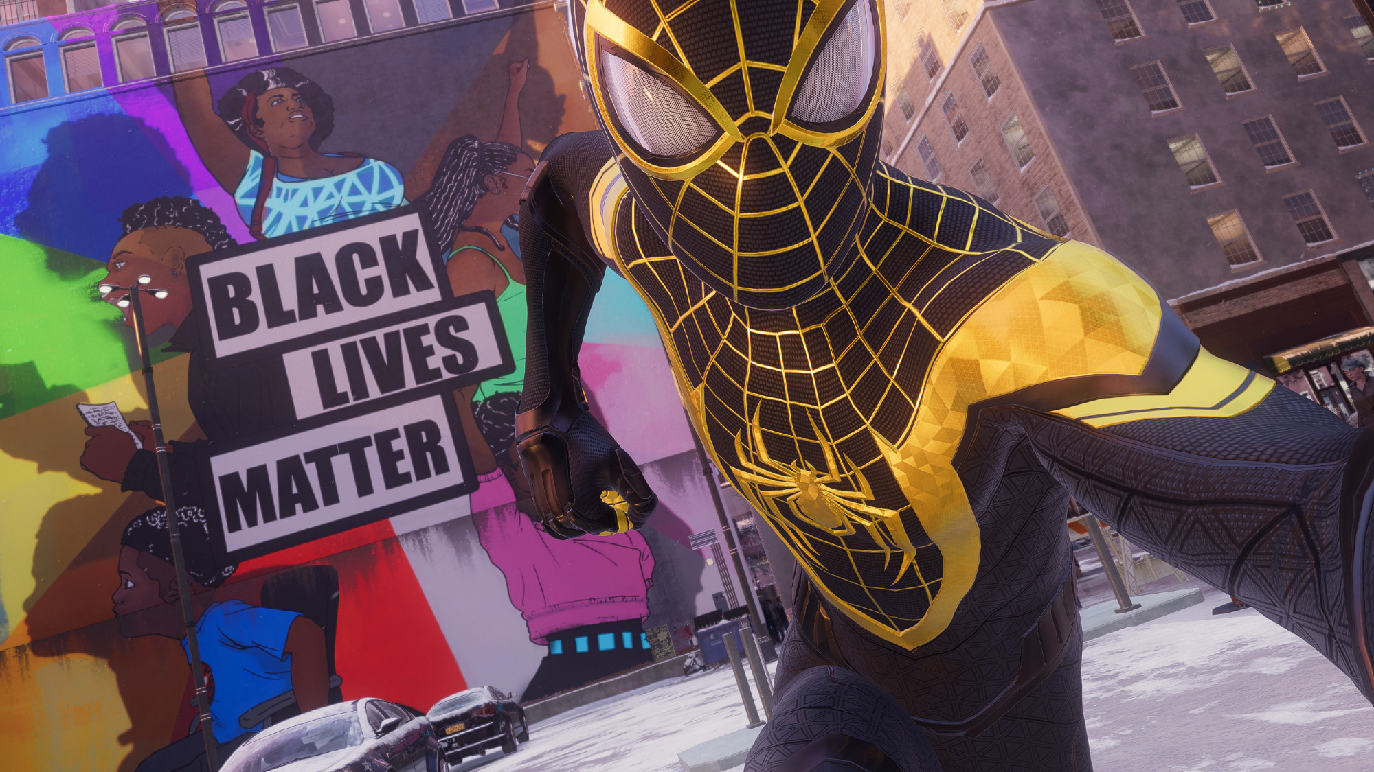 Spider-Man posing in front of a Black Lives Matter mural in New York City, while wearing a black and gold inspired suit.