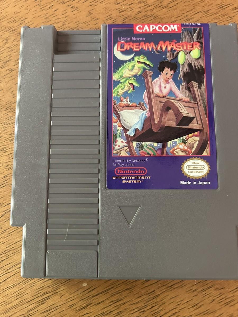 NES cartridge on a table, the game is Little Nemo: Dream Master. A boy is riding a flying bed through a town, a scary alive tree in the background, alligators flying near a crescent moon.