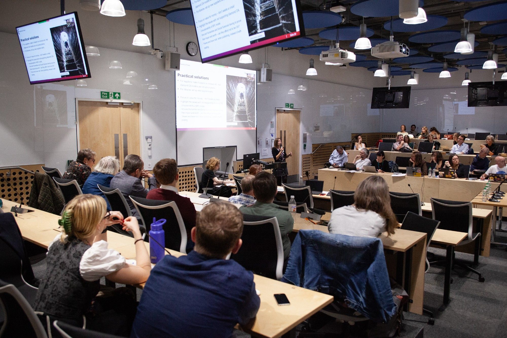 A view of from the back of the lecture theatre, showing the audience and a speaker