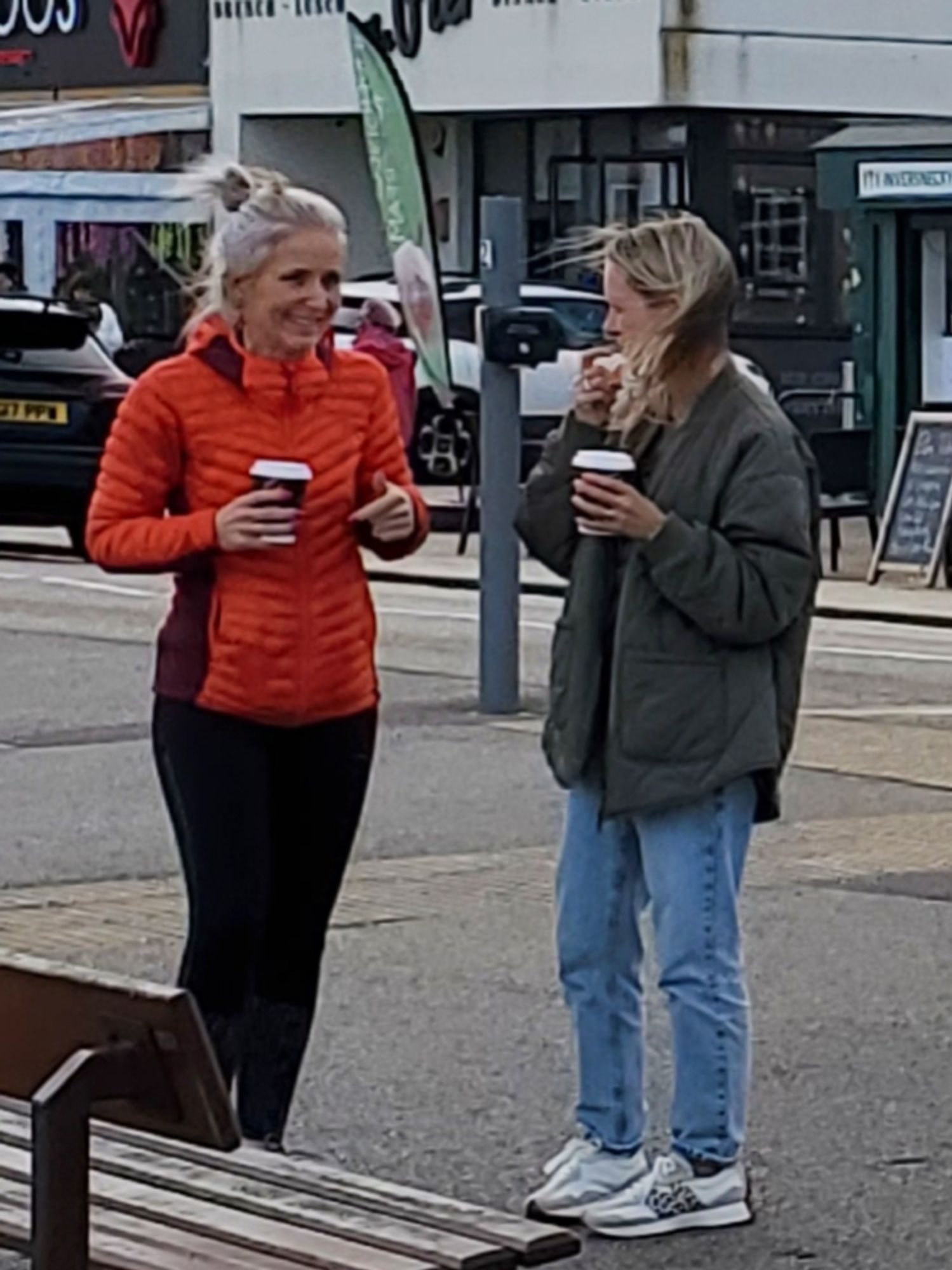 2 women in deep discussion whilst drinking coffee by the side of the street.