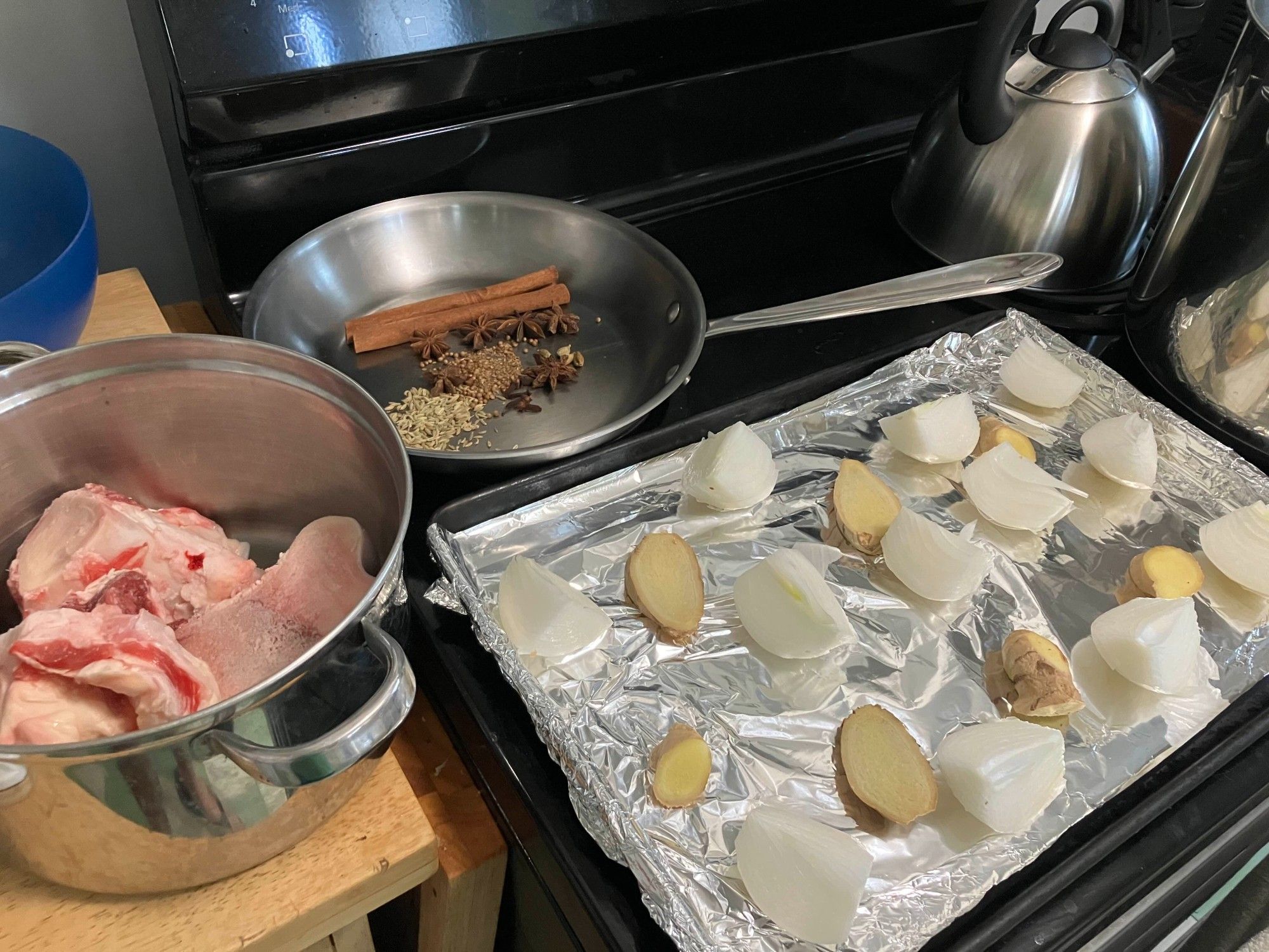 herbs in a pan to be warmed, beef bones, and a broiler pan of ginger and onions.