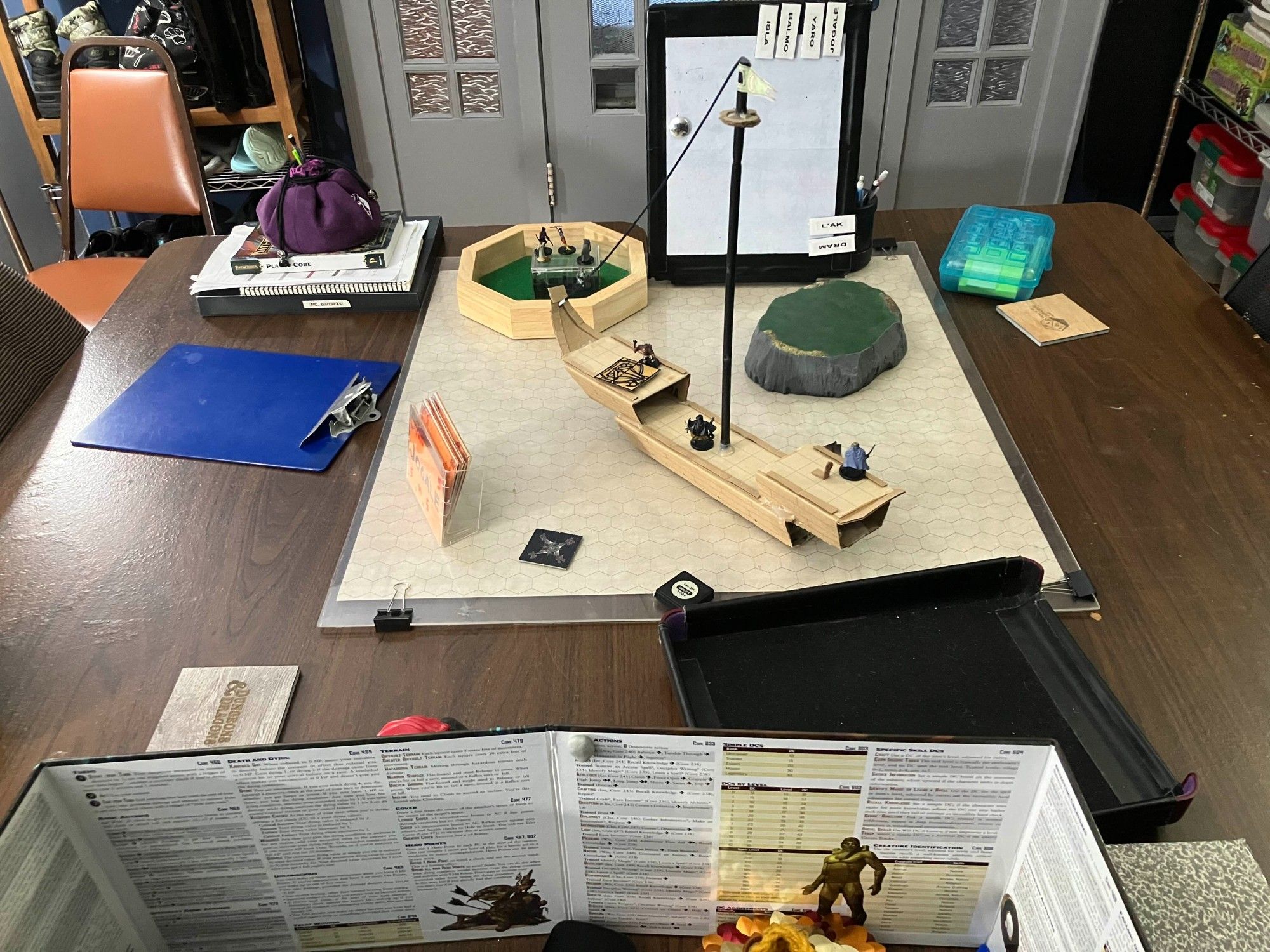 Players' seats and table set up with a cardboard boat, miniature figures, terrain and a dry erase board for tracking initiative.