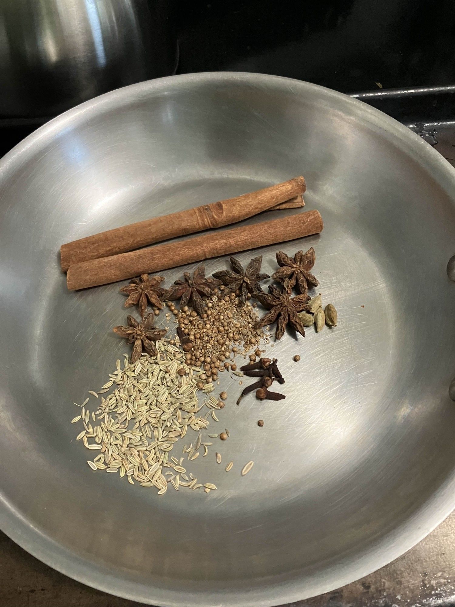 Cinnamon, star anise, fennel, cardamom, and coriander seeds in a pan to be warmed.