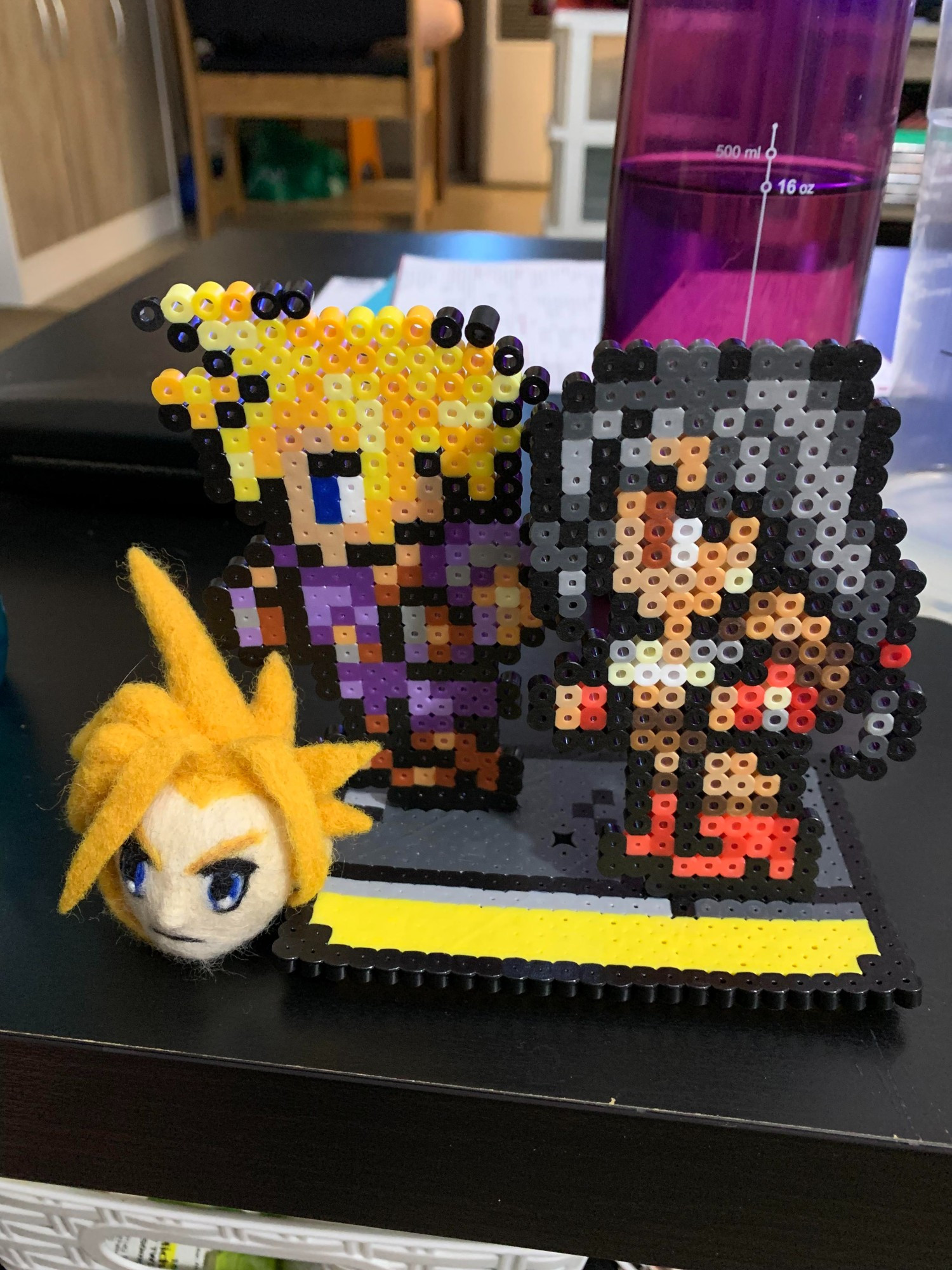 Needle felted head of Cloud Strife, circa his original, blocky appearance from '97, in front of a perler bead pixel diorama of Tifa and Cloud.