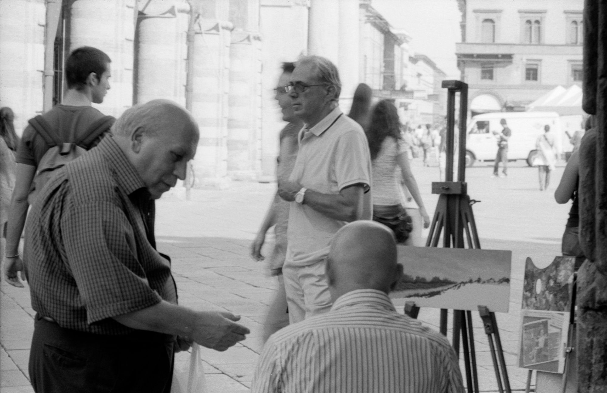 Two gents having a discussion on the edge of a public square, with one of them sitting at an easel, painting a snowy landscape as the general public walks by, Piazza Maggiore, Bologna, Italy, 2012.