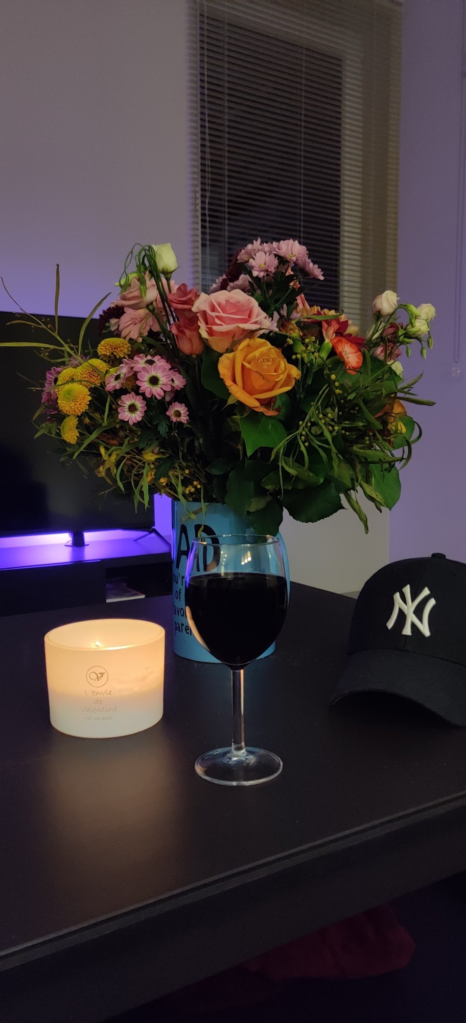 Un verre de vin sur une table de salon a côté d'une bougie et devant un magnifique bouquet de fleurs multicolores.