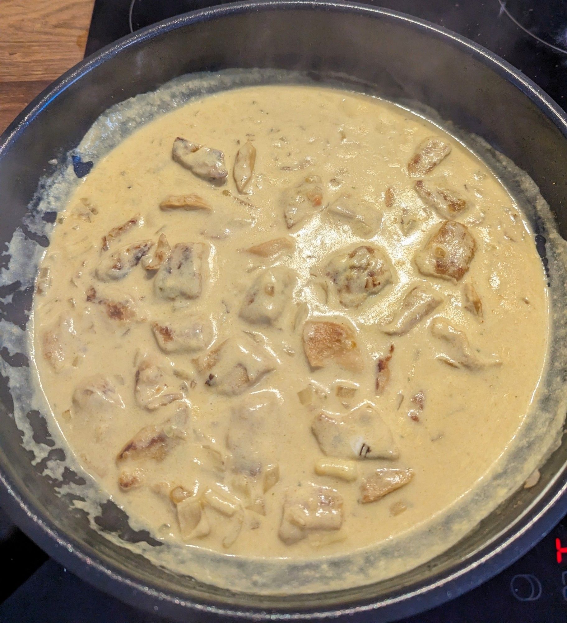 Eine Pfanne steht auf dem Herd. Darin befindet sich das gelbe Curry. Die braunen angebratenen Planted-Stücke sind deutlich in der Soße zu sehen.