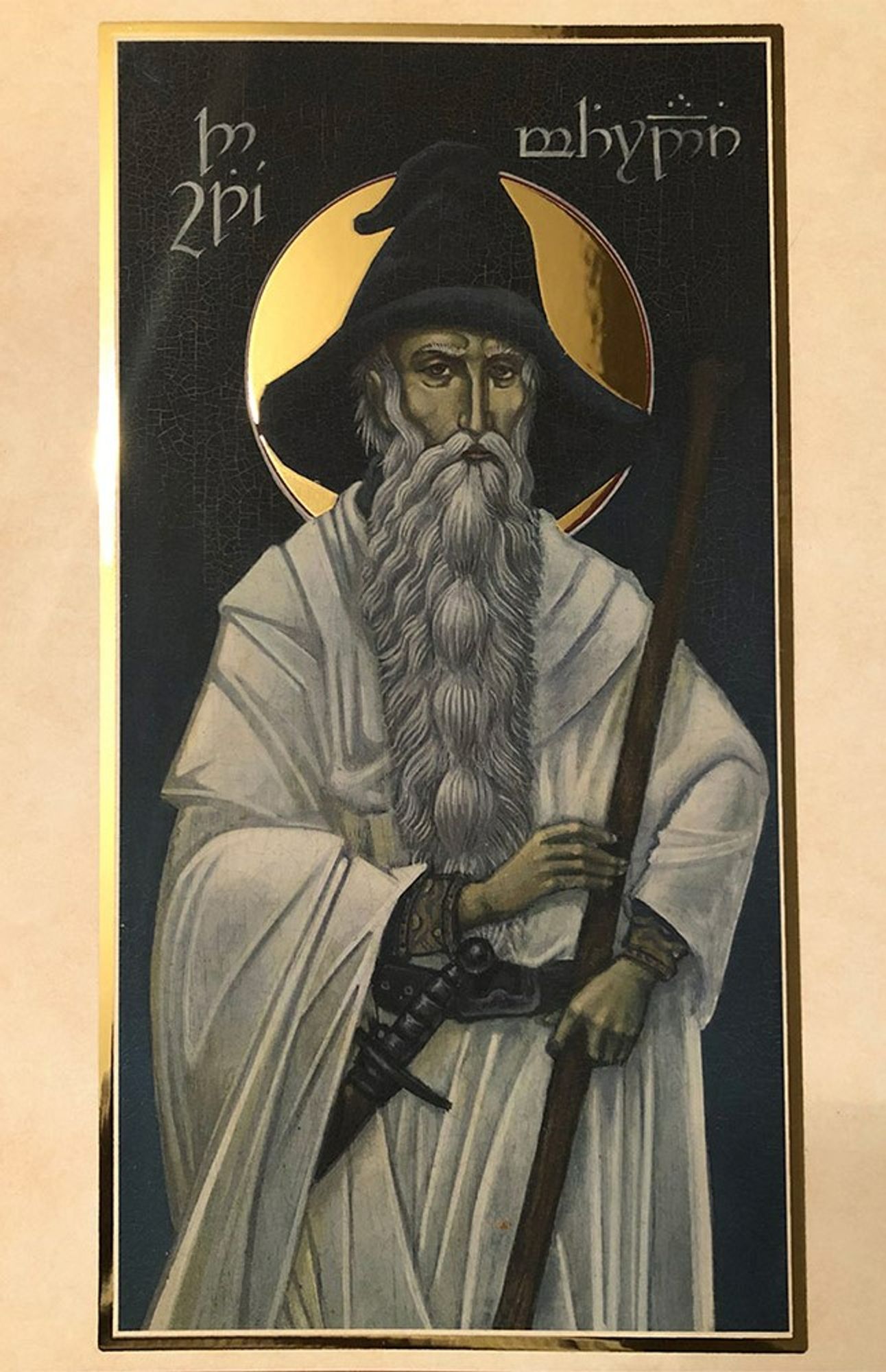 A painting of the wizard Gandalf from The Lord of the Rings in the style of a traditional Byzantine icon. Gandalf, looking like a proper Desert Father except  for the sword at his belt and the wizard's hat on his head, has a halo and is wearing a white robe.