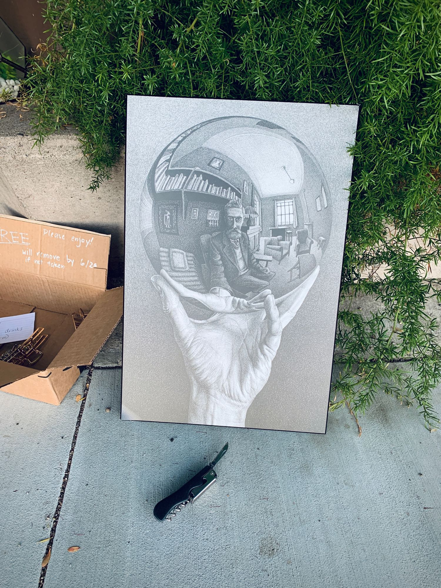 An MC Escher self portrait with sphere, and a pocketknife, on the sidewalk next to a free sign written on cardboard