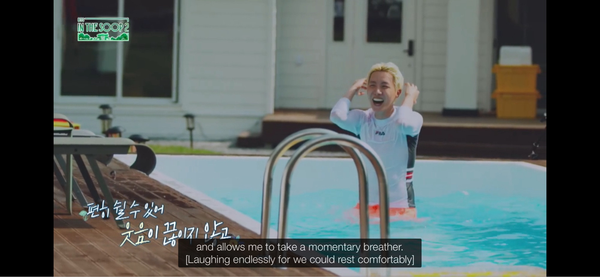 Jhope standing in a swimming pool in a white, long sleeved rash guard and pink swim trunks. He’s brushing his blonde hair back with both hands and smiling widely. The subtitle says “and allows me to take a momentary breather. [Laughing endlessly for we could rest comfortably].”