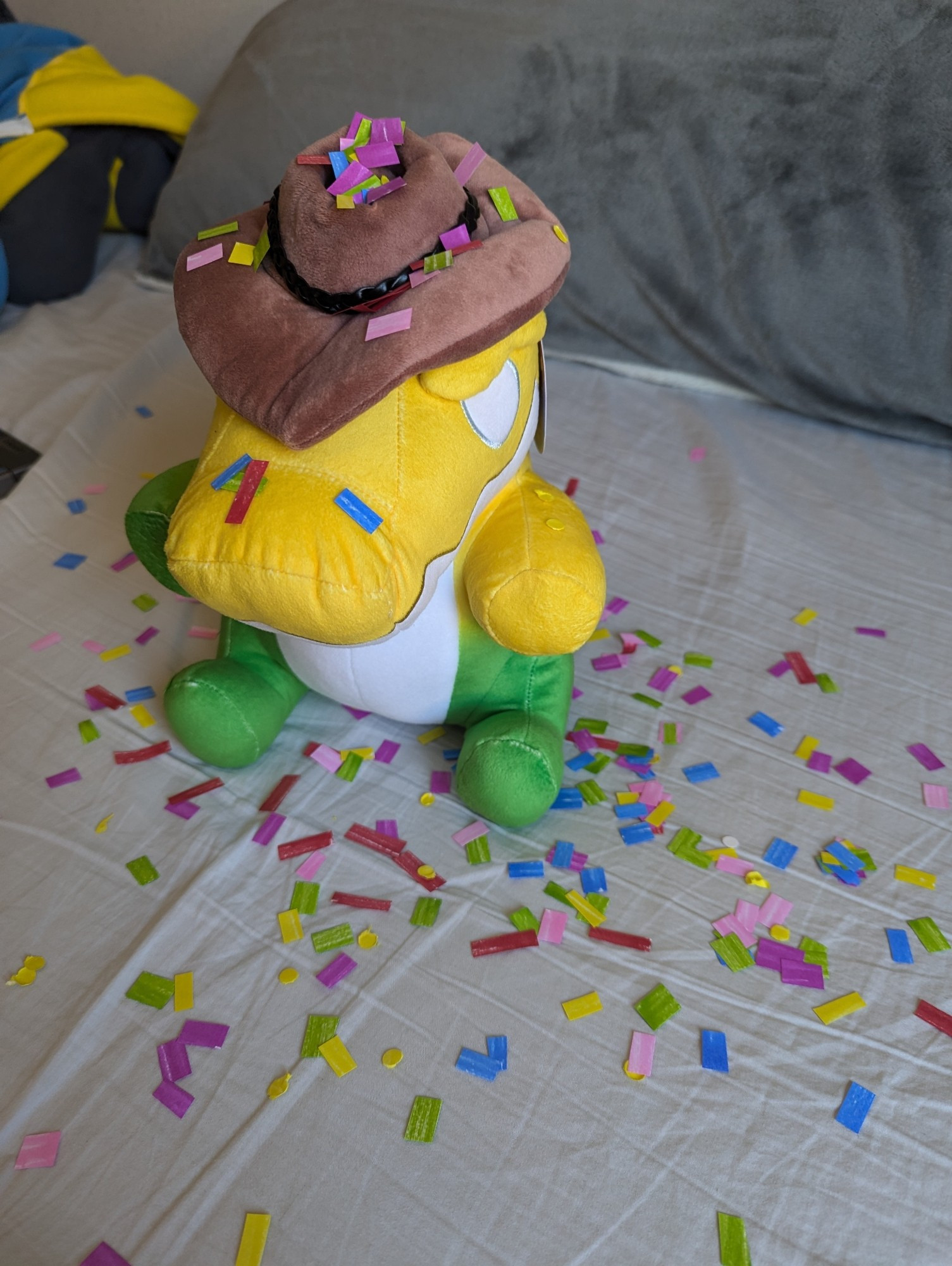 Reverse shot of the sitting Gummigoo Plush, showing off more of the confetti around and some confetti on his hat