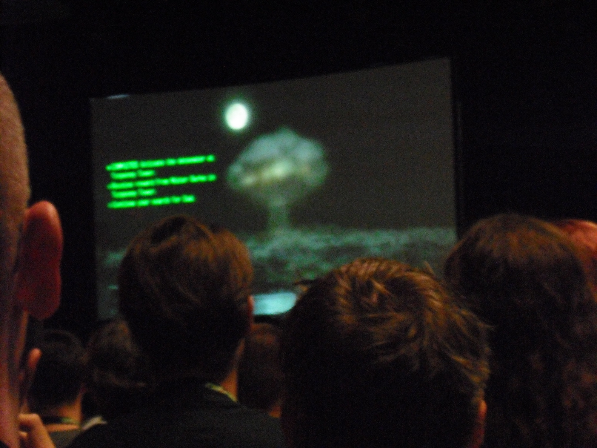 Auditorium, back of heads, and a huge screen showing a mushroom cloud as Megaton is blown up.