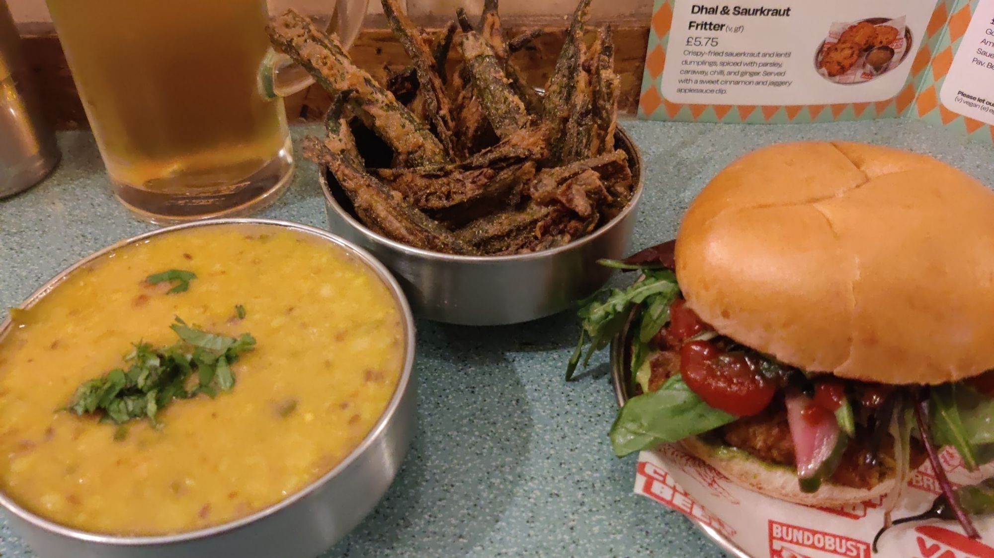 A photo of some lentil dal, a bhaji butty and some okra fries. The bottom half of a pint is in the background