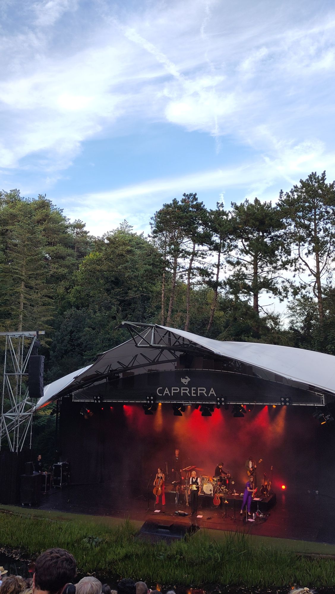 Open air stage with band in red lights and blue sky and clouds above
Openluchtpodium met band in rood licht en blauwe wolkenlucht erboven