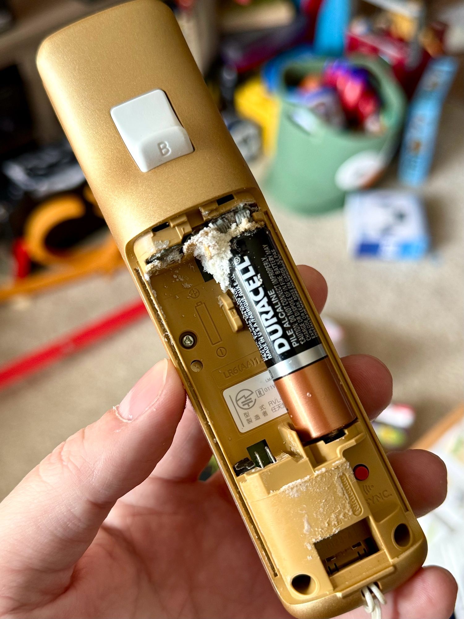 The open battery compartment of a gold Wii Remote, where a battery has leaked acid all over the dang place and now it's caked on the contacts and stuff.