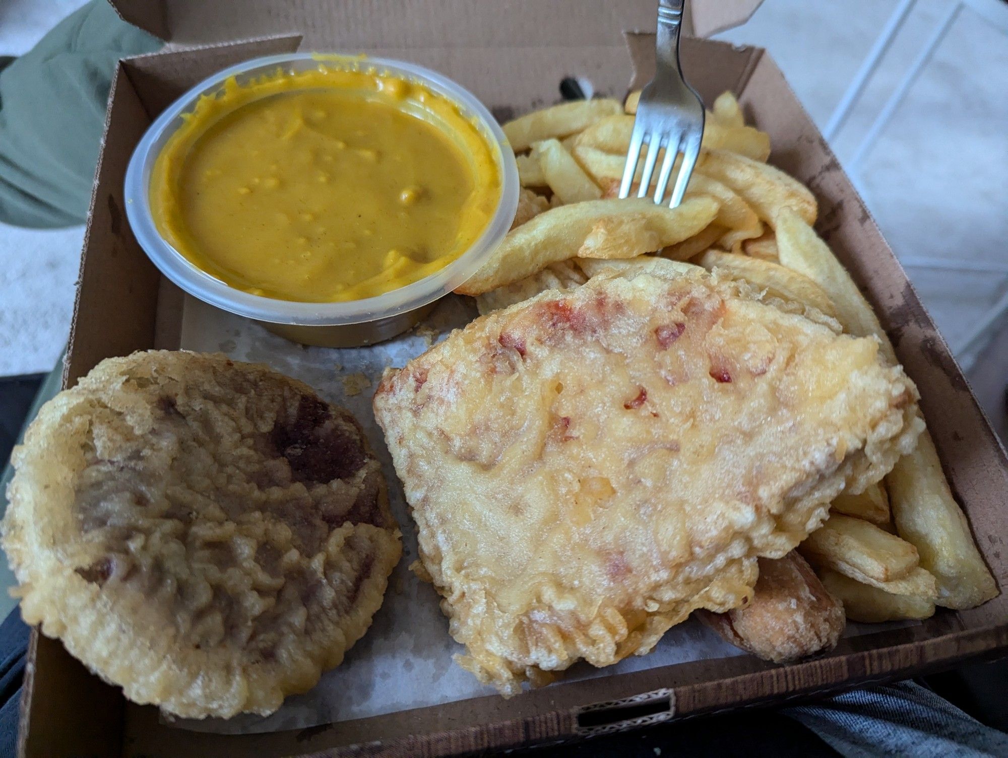 A box of food from a Scottish chip shop. Visible clockwise from top left: chip shop curry sauce, chips, pizza crunch (deep fried battered pizza), and a deep fried battered hamburger patty.