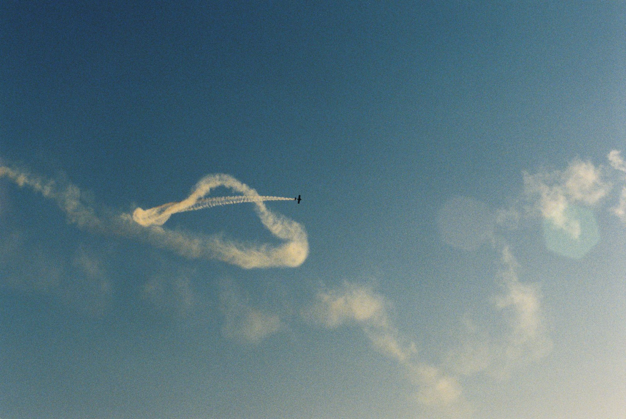 A film photo of a aerobatic plane, mainly focusing on the smoke trails left behind.