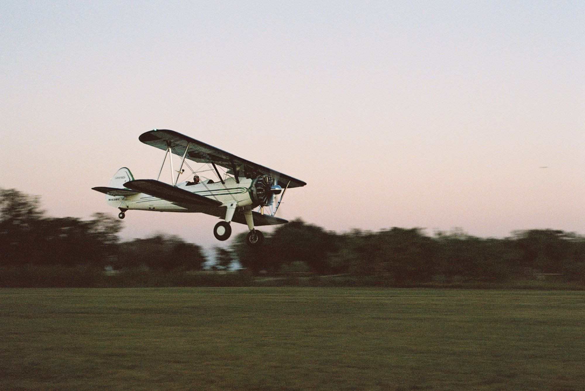 A landing white-and-green biplane shot against sunset. 