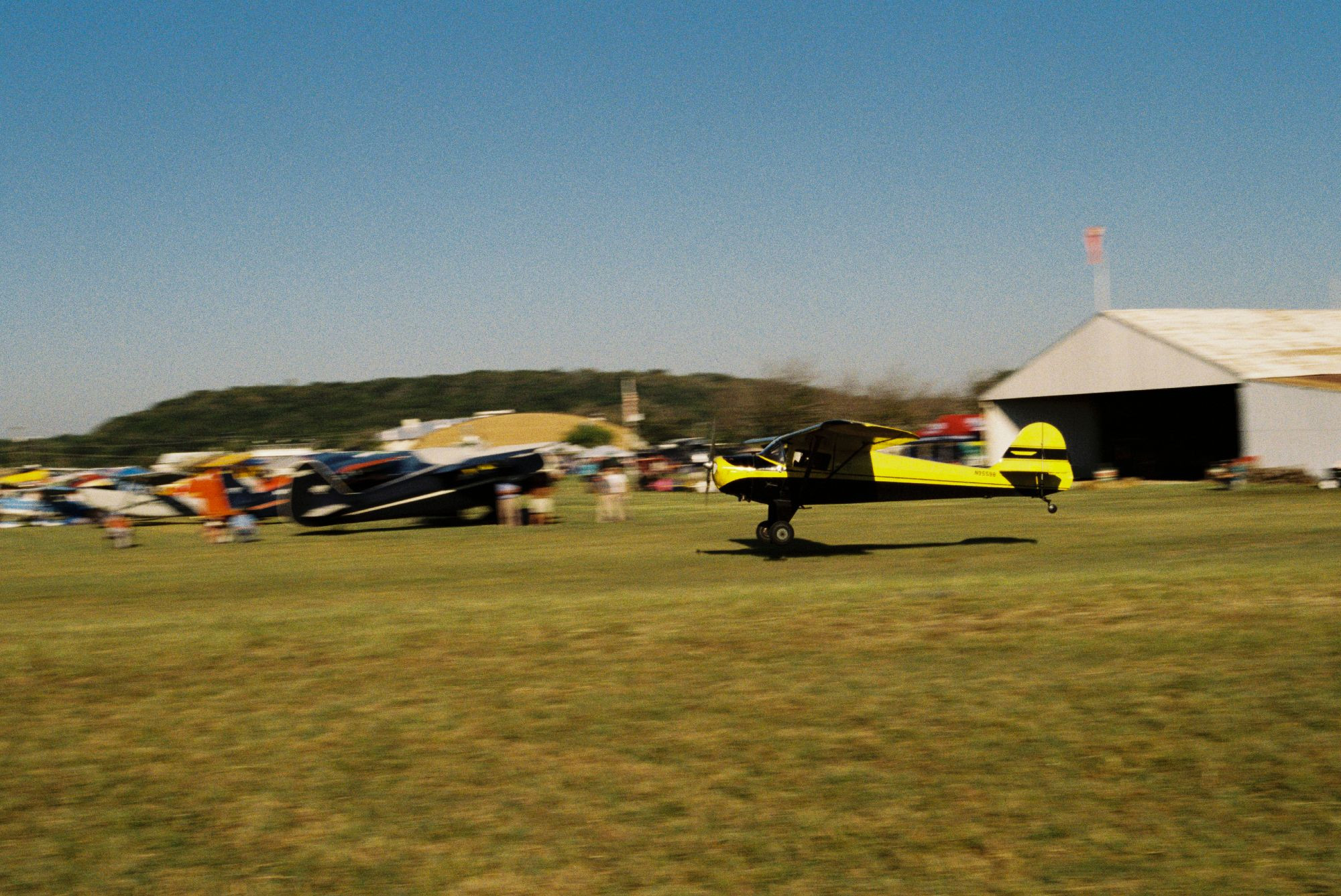 A yellow and black plane landing on a grass field, a background of planes blurred in the background.