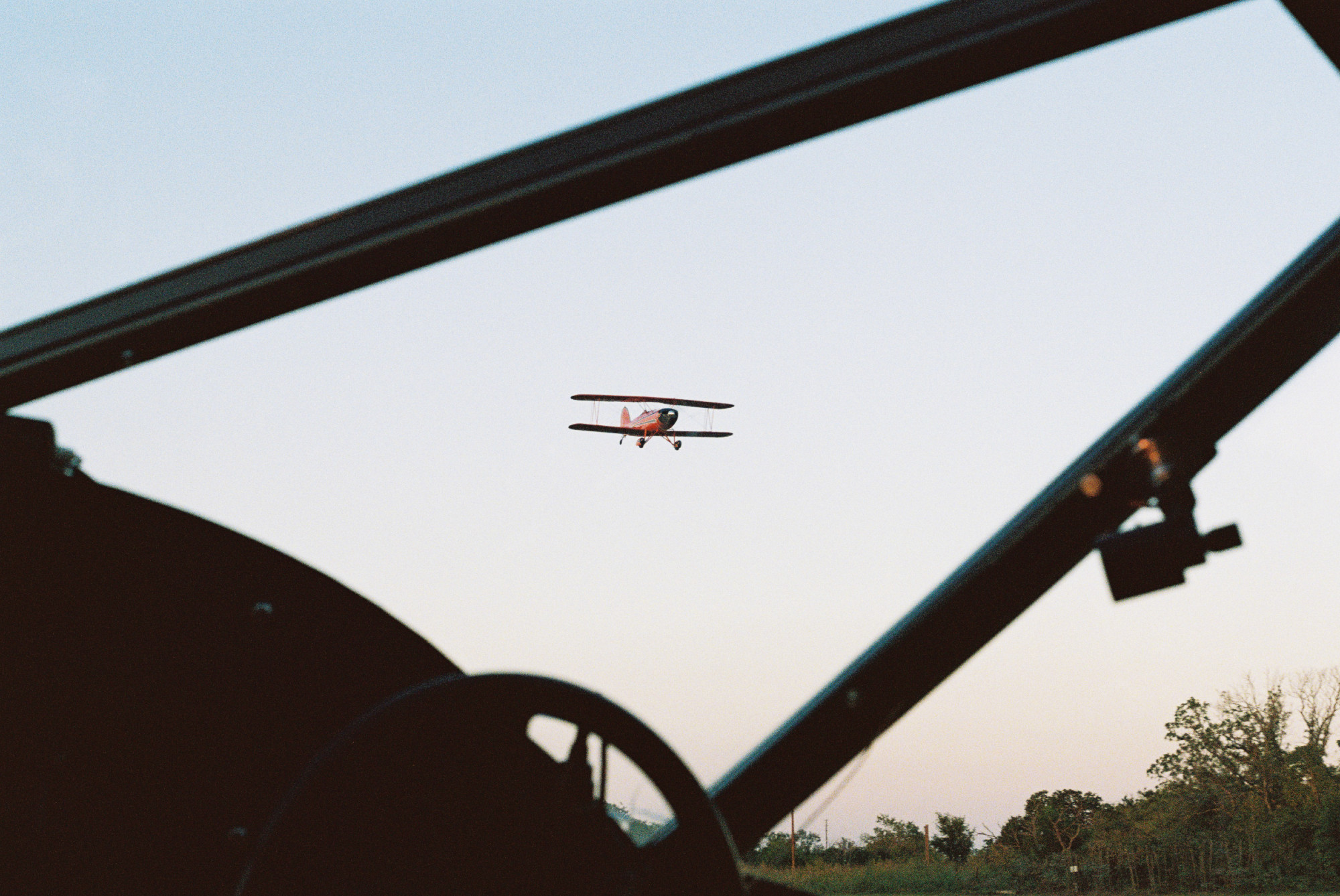 A film photo of a landing biplane shot through the windshield of a different plane.