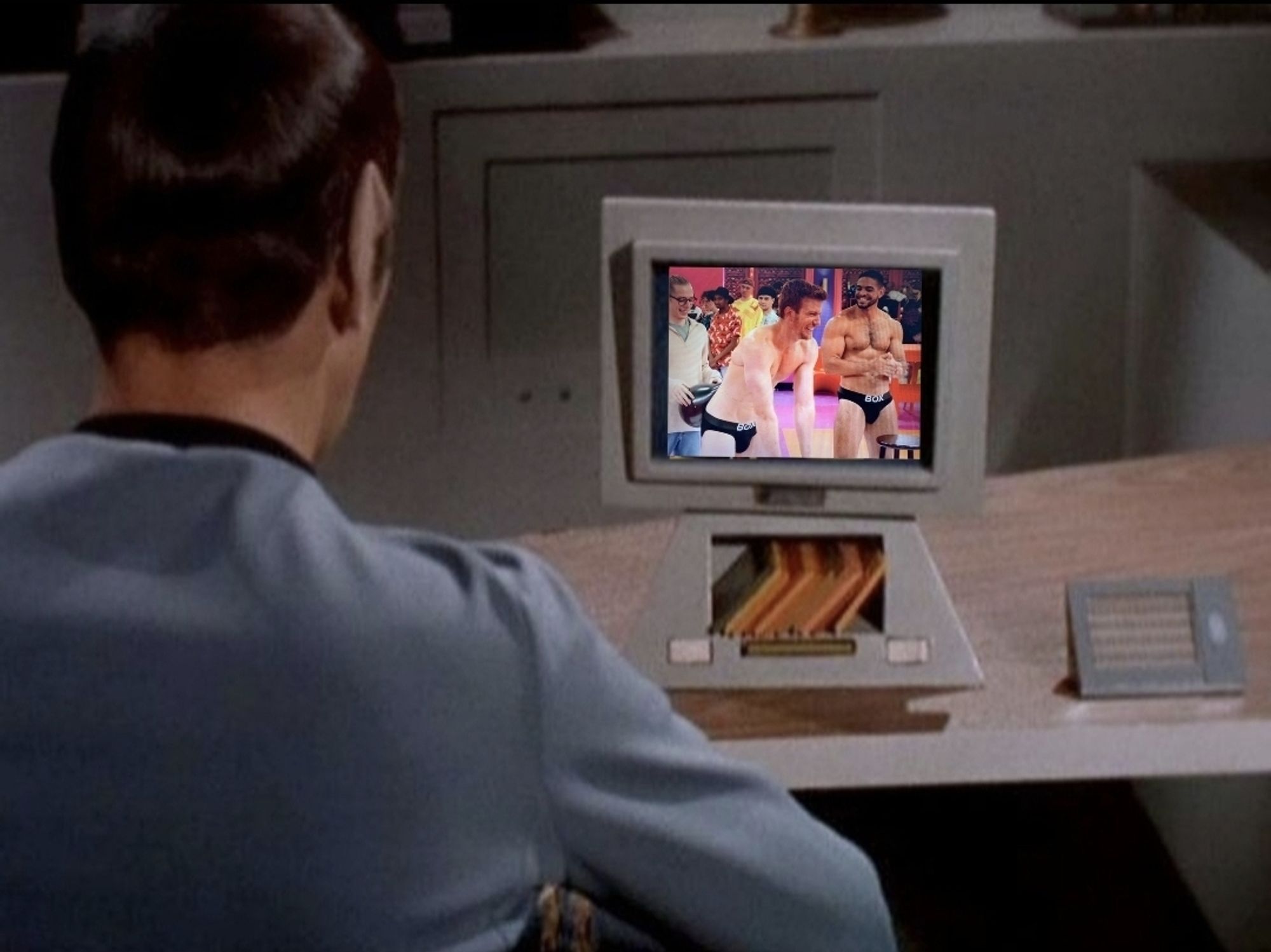 Edited screenshot from an episode of Star Trek TOS The Original Series, of Spock sitting at a desk as seen from behind. He is looking at a computer monitor mounted to the desk,  which has a compartment that looks like it's holding memory discs of some kind. We see what Spock is looking at on the computer: he is watching the pit crew in their underwear during a mini challenge on an episode of RuPaul's Drag Race, Season 14.