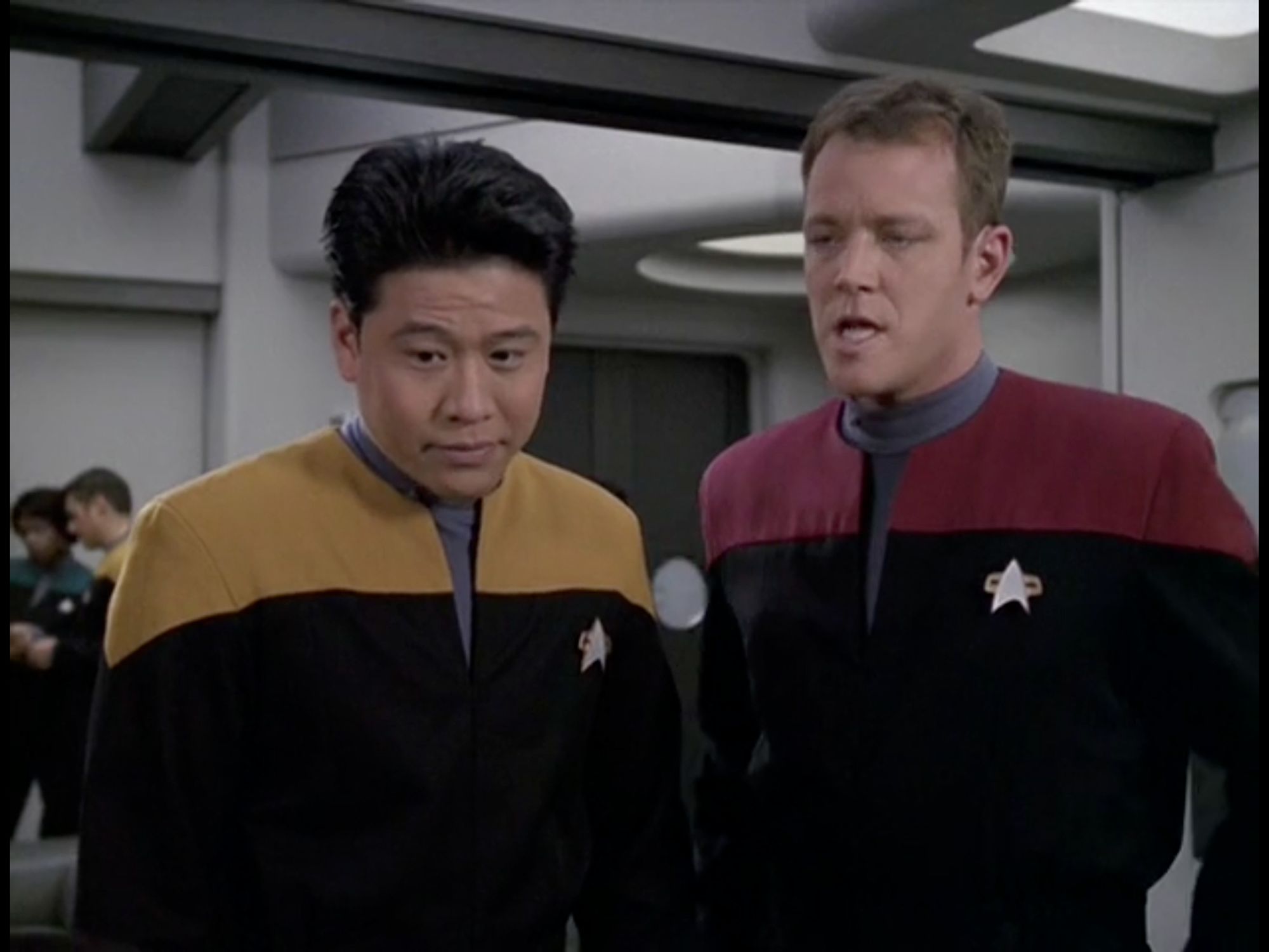 Harry is now looking down with his eyebrows raised, with a smug expression, as though he just won an argument. His arms are now down by his sides. Tom is standing straight up next to him, his eyes are half closed, and he is jutting out his chin with his mouth is open, giving him a slight neanderthal appearance. 

From Star Trek Voyager, Season 6, Episode 11, "Fair Haven"